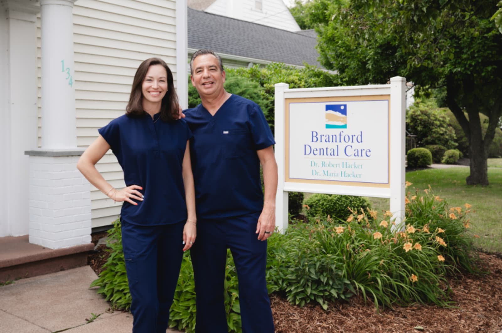 Two team members in navy scrubs standing together outside Branford Dental Care office