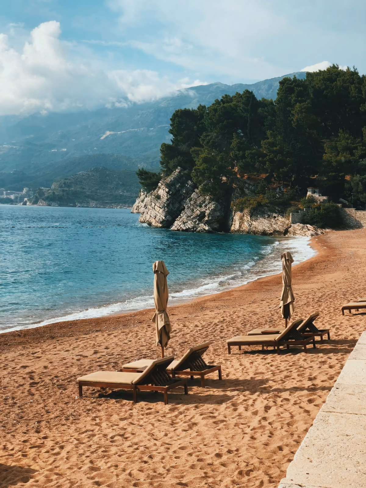 Adriatic beach with sun loungers below wooded cliffs