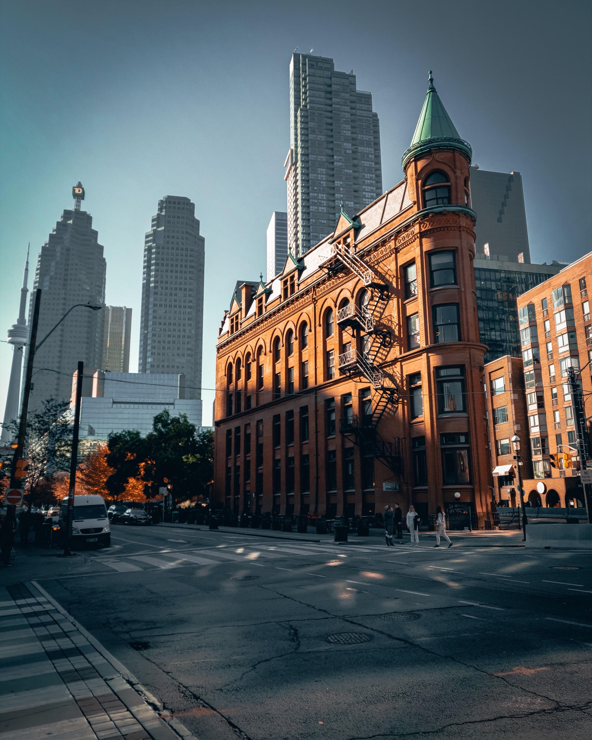 Toronto street corner at golden hour, with the red brick Gooderham Building and the downtown financial district behind it.