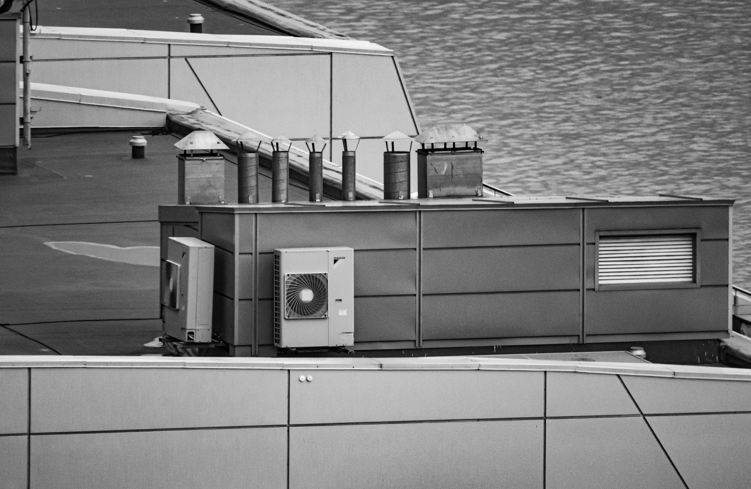 Rooftop mechanical plant in black and white: a condenser unit, exhaust vents and a screened enclosure on a commercial roof.