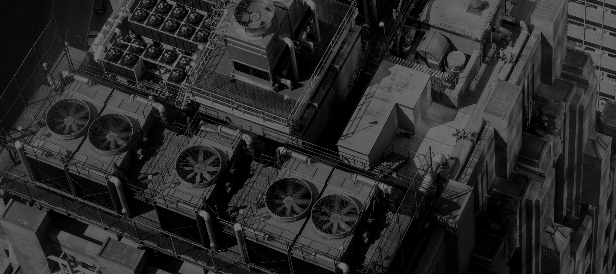 Aerial view in black and white of a commercial rooftop plant: banks of cooling tower fans, condenser units and pipework.