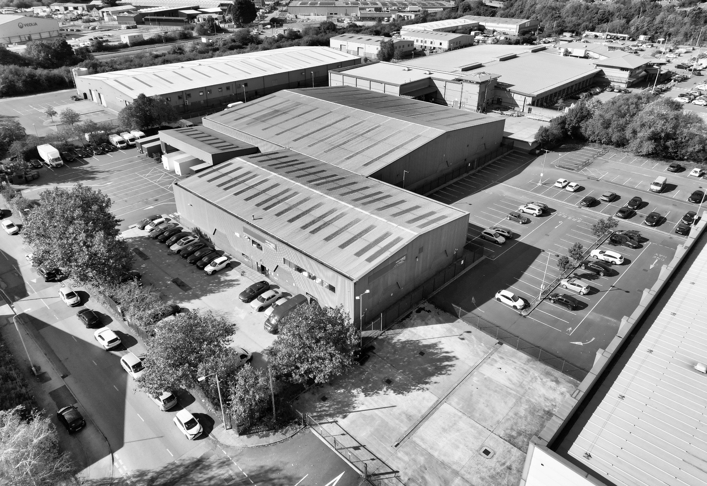 Aerial view in black and white of a distribution warehouse and trade counter estate, with loading bays and parking.