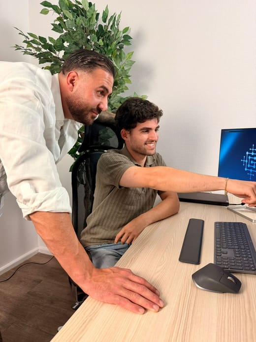 Zwei Mitarbeiter des GG IT-Systemhauses am Arbeitsplatz — einer erklärt dem anderen etwas am Bildschirm
