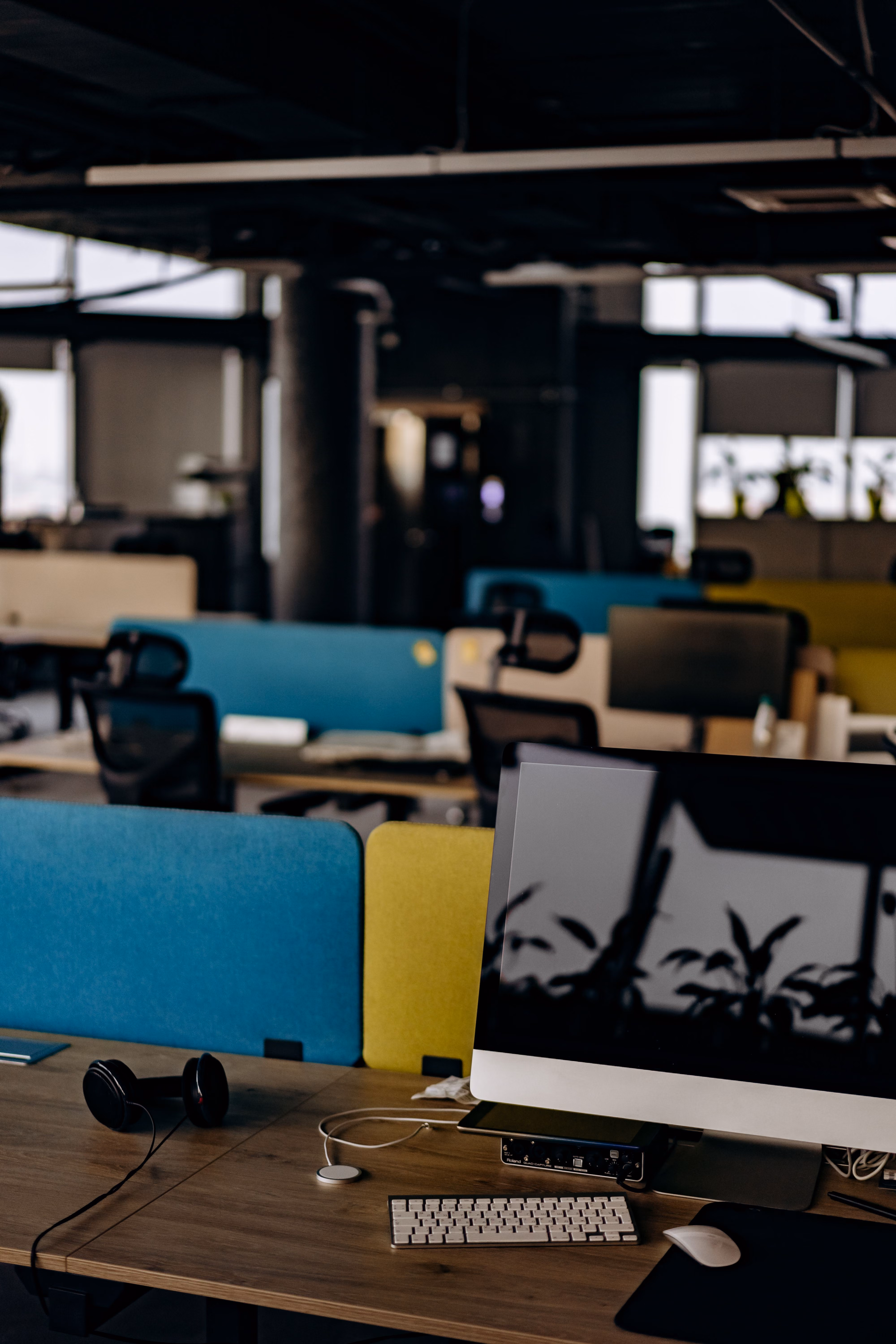 Büro mit Arbeitsplätzen, im Vordergrund ein Monitor mit Tastatur und Kopfhörern