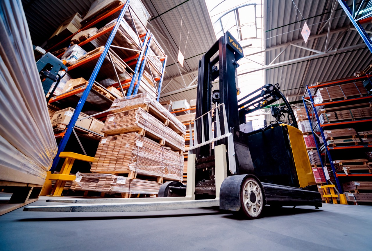 Black and yellow Yale forklift in a warehouse with stacks of wood and metal shelving.