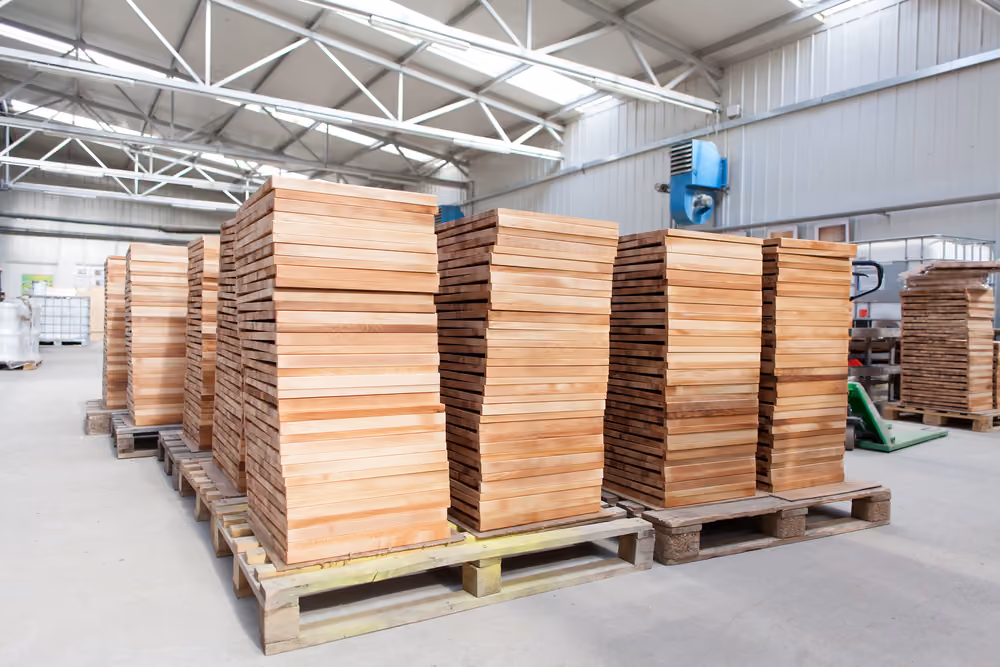 Stacks of rectangular wooden planks on pallets inside a large industrial warehouse.