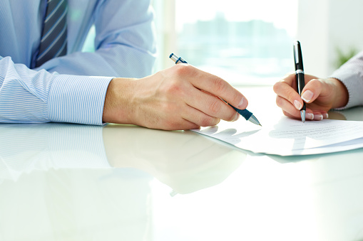 Close-up of people writing/signing a document