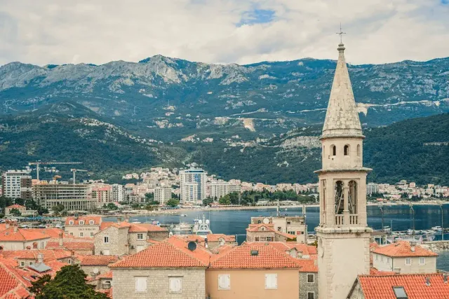 Croatian coastal town with red-tiled roofs, a church bell tower and mountains behind