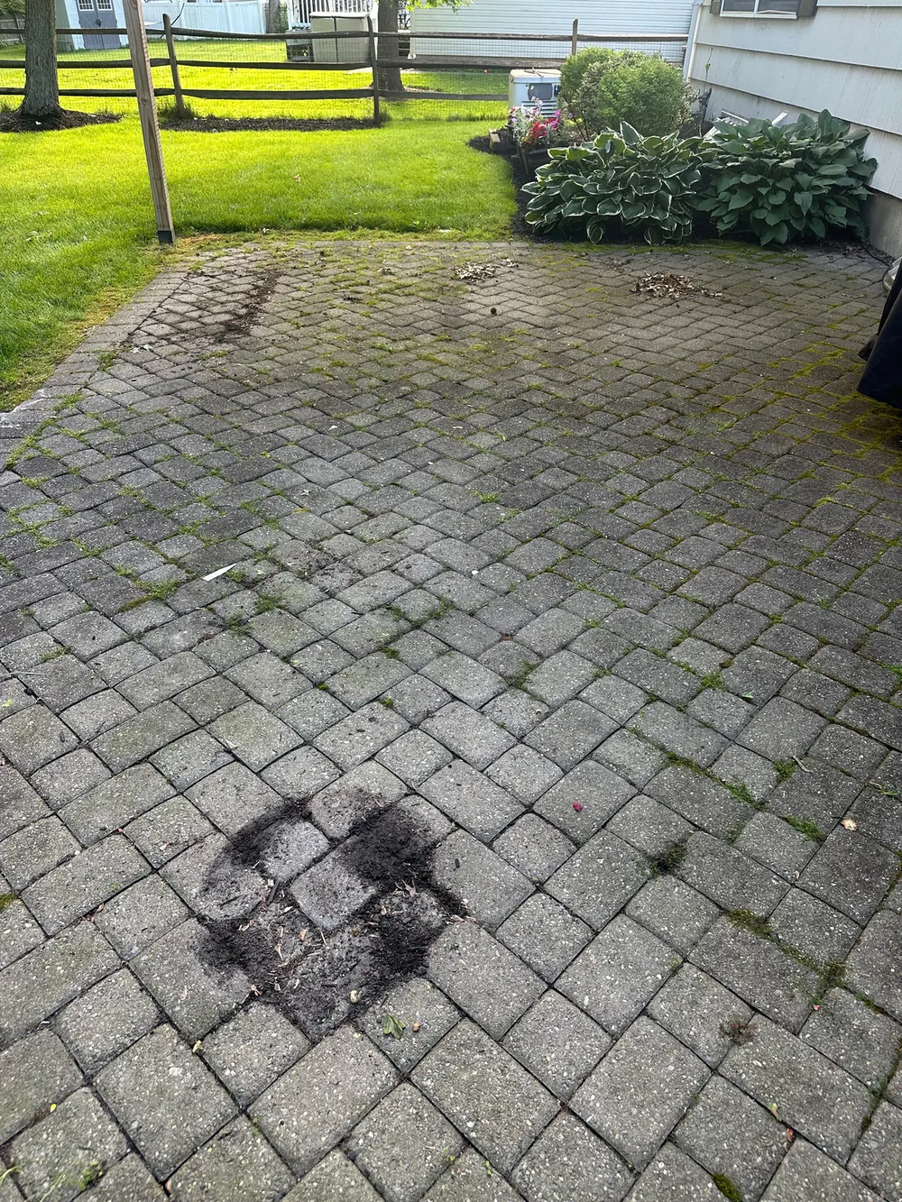 Gray paver patio with moss in the joints and a dark scorch stain