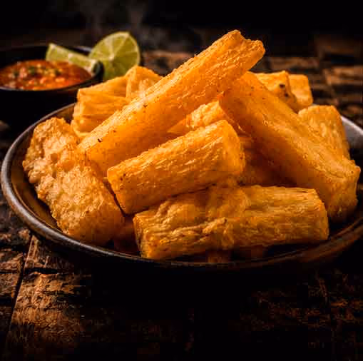Plate of crispy fried yuca sticks with lime wedges and sauce in the background.