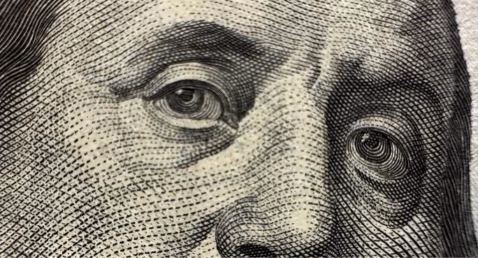 Close-up of detailed eyes and nose on a U.S. hundred-dollar bill portrait.