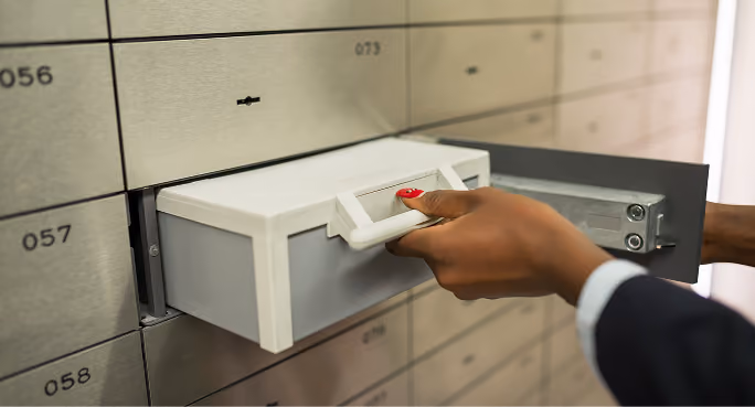 Hand with red nail polish pulling out a small safe deposit box from a safety deposit locker.