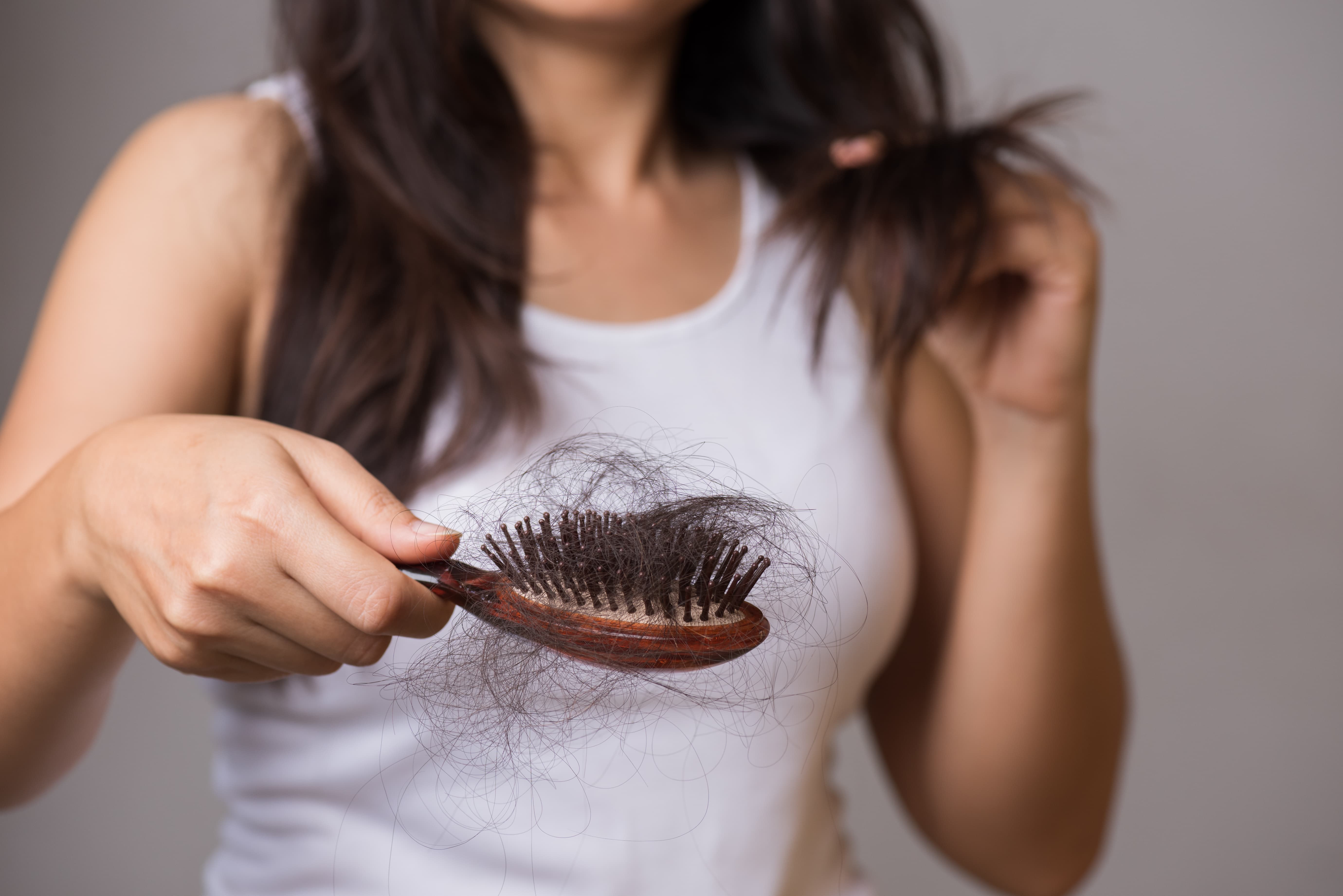 Woman examining thinning hair, illustrating a root-cause approach to hair restoration