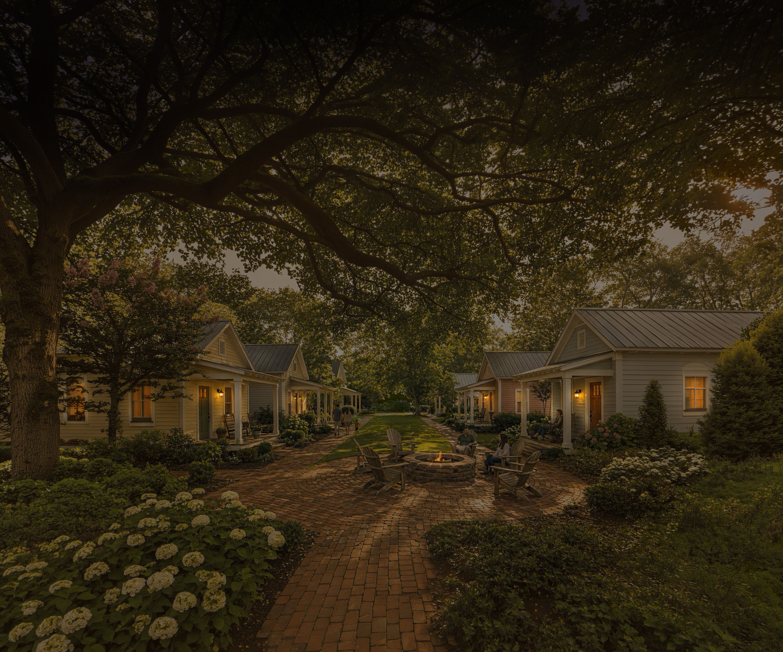 Cozy cottages with porches around a fire pit amid brick paths and lush greenery under large trees.