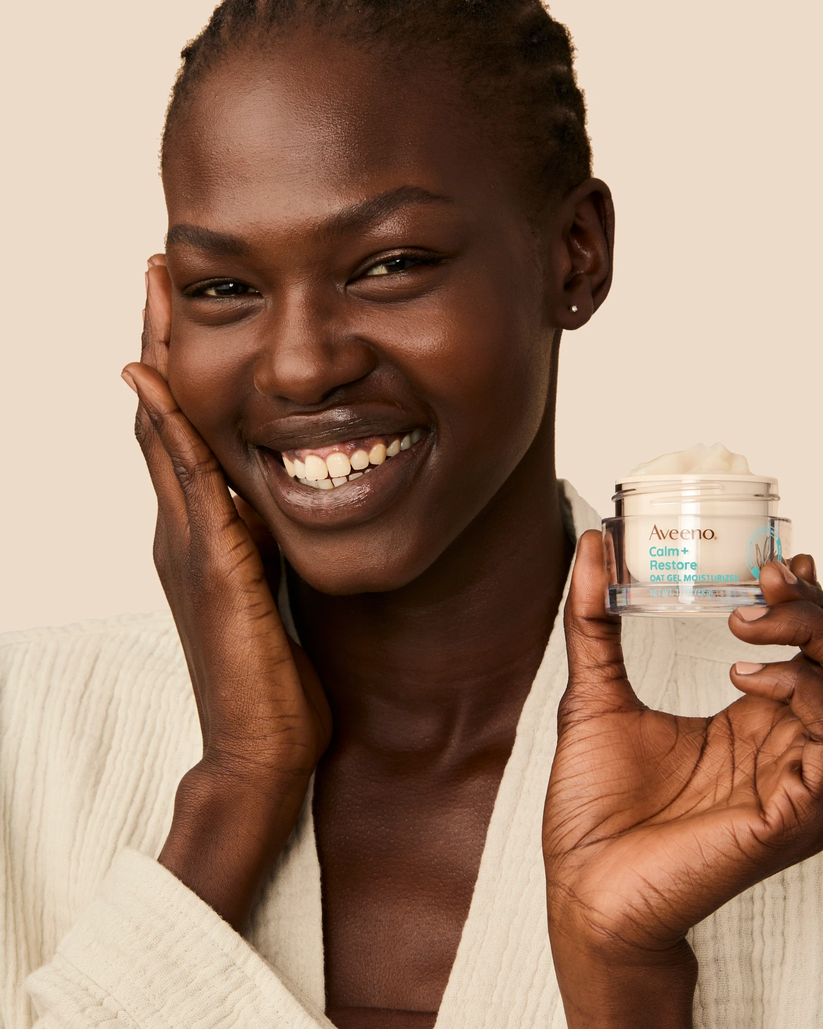 A smiling model holding an Aveeno jar beside her face.