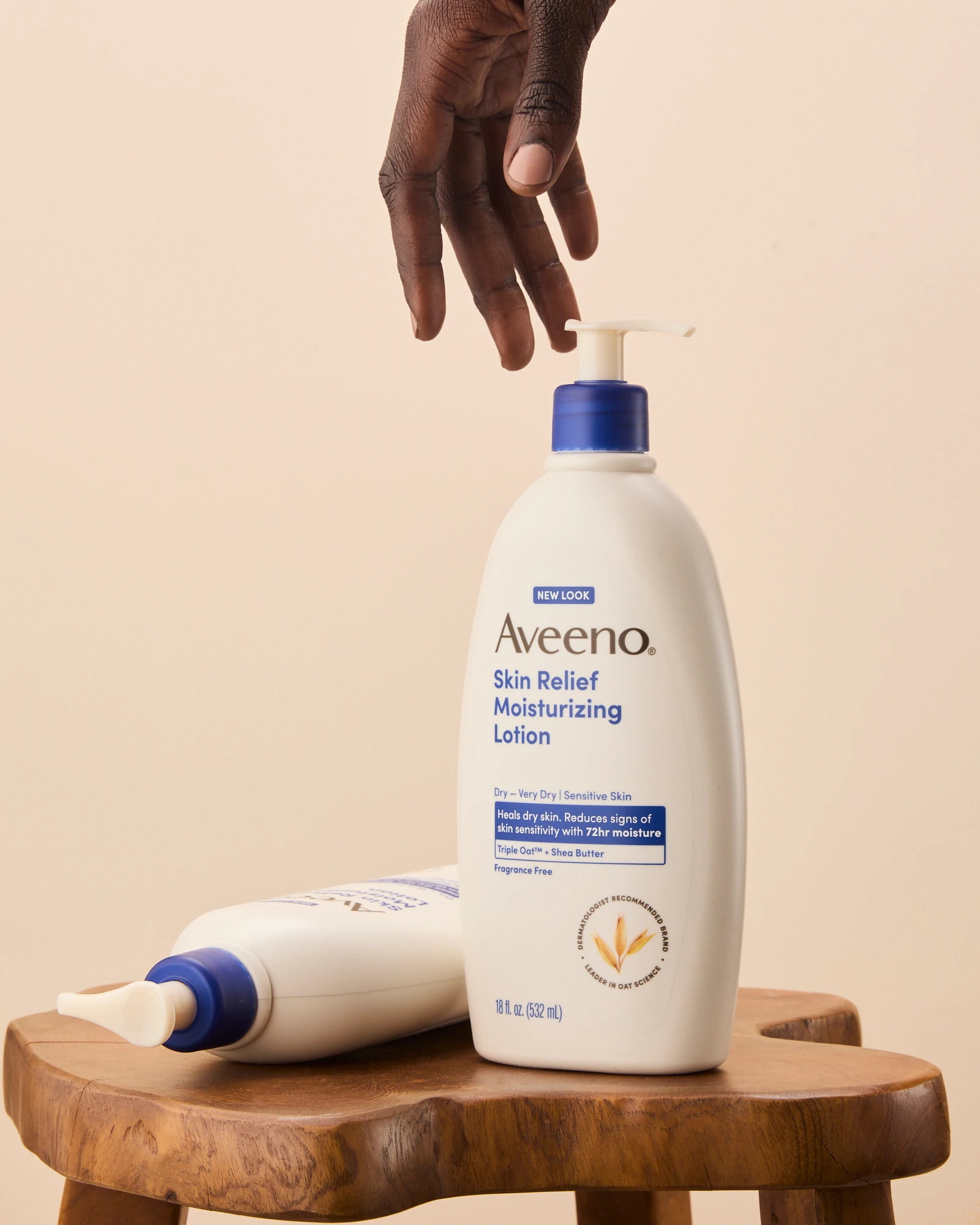 A hand reaching toward an Aveeno pump bottle.