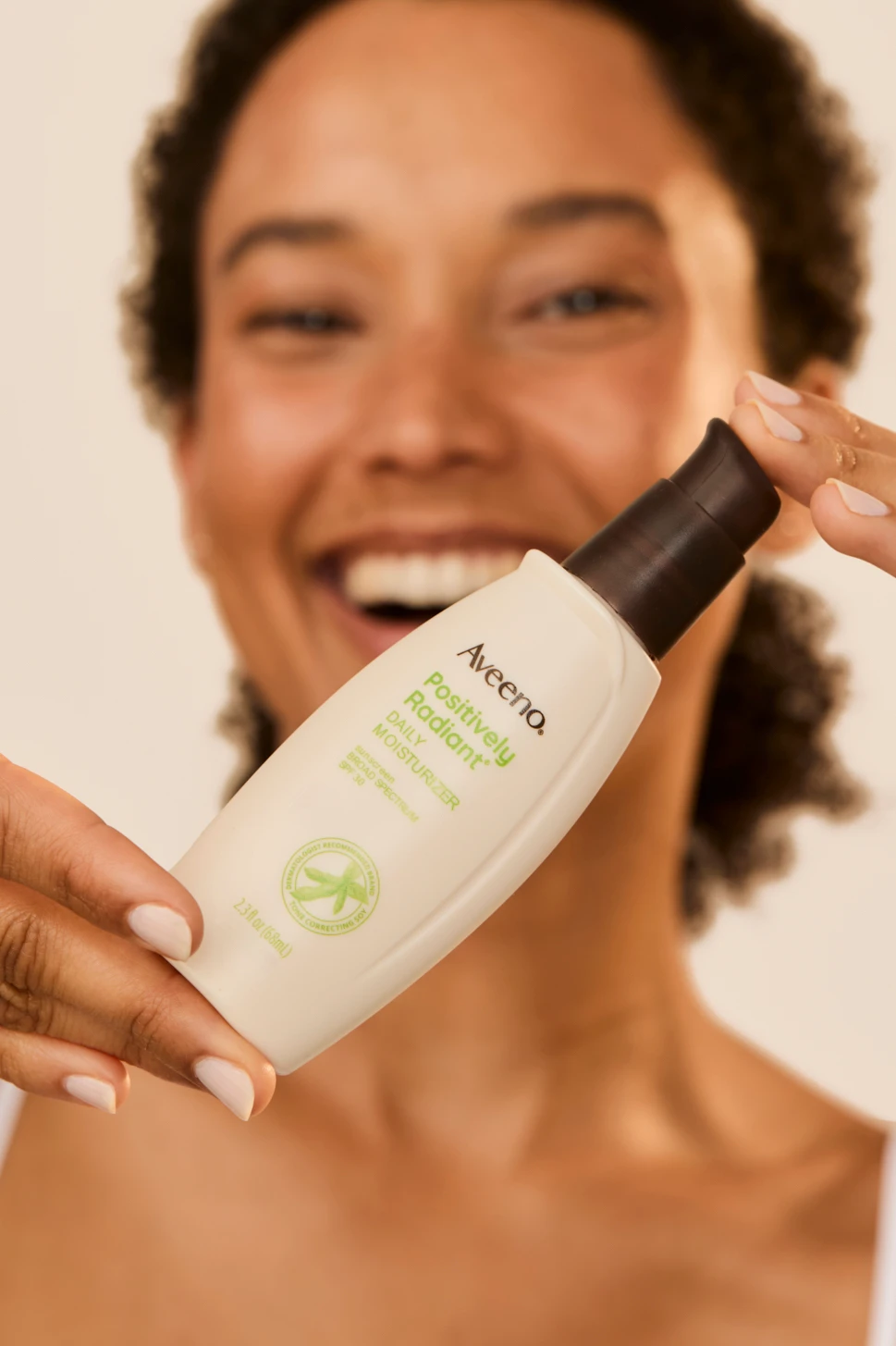 A model presenting an Aveeno bottle toward the camera.