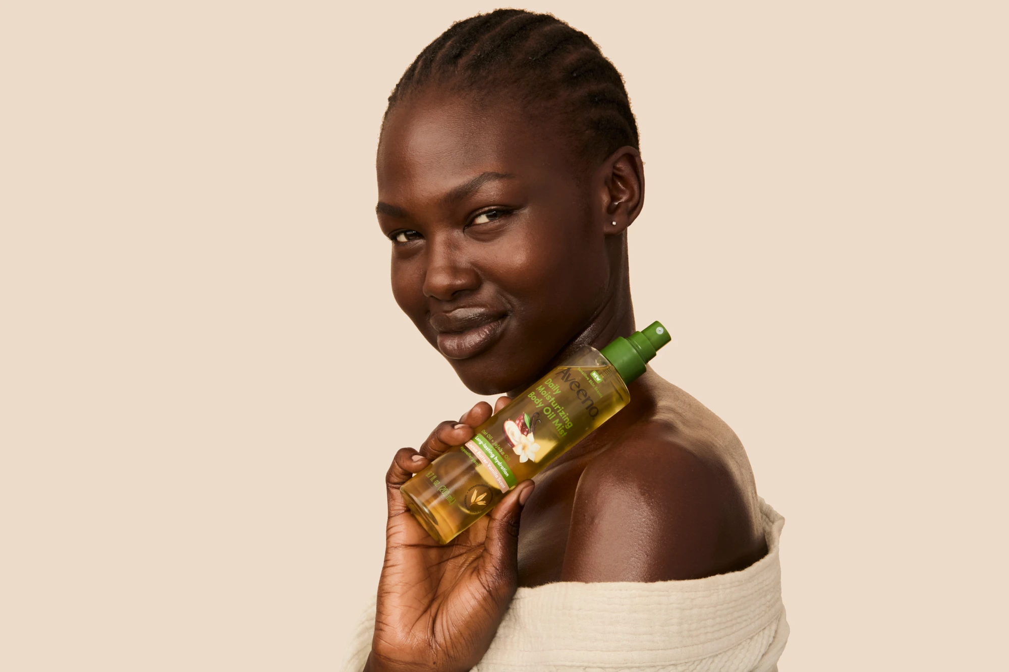 A model holding an Aveeno oil bottle beside her shoulder.