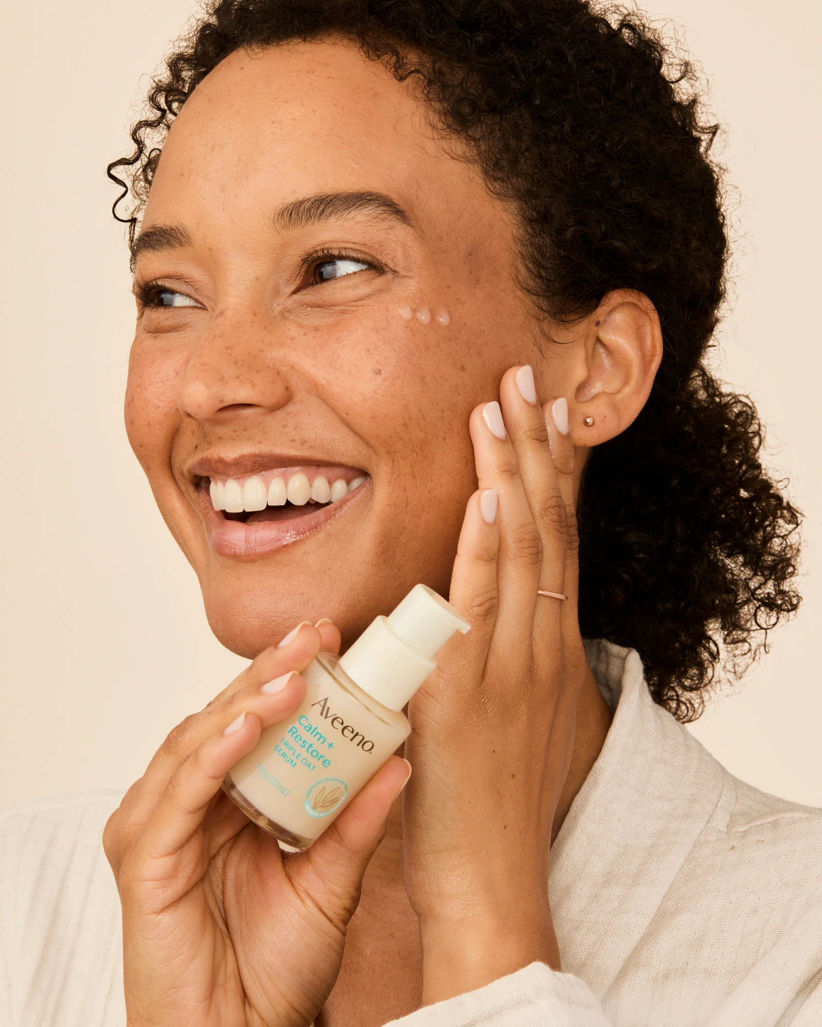 A smiling model applying product to her cheek.