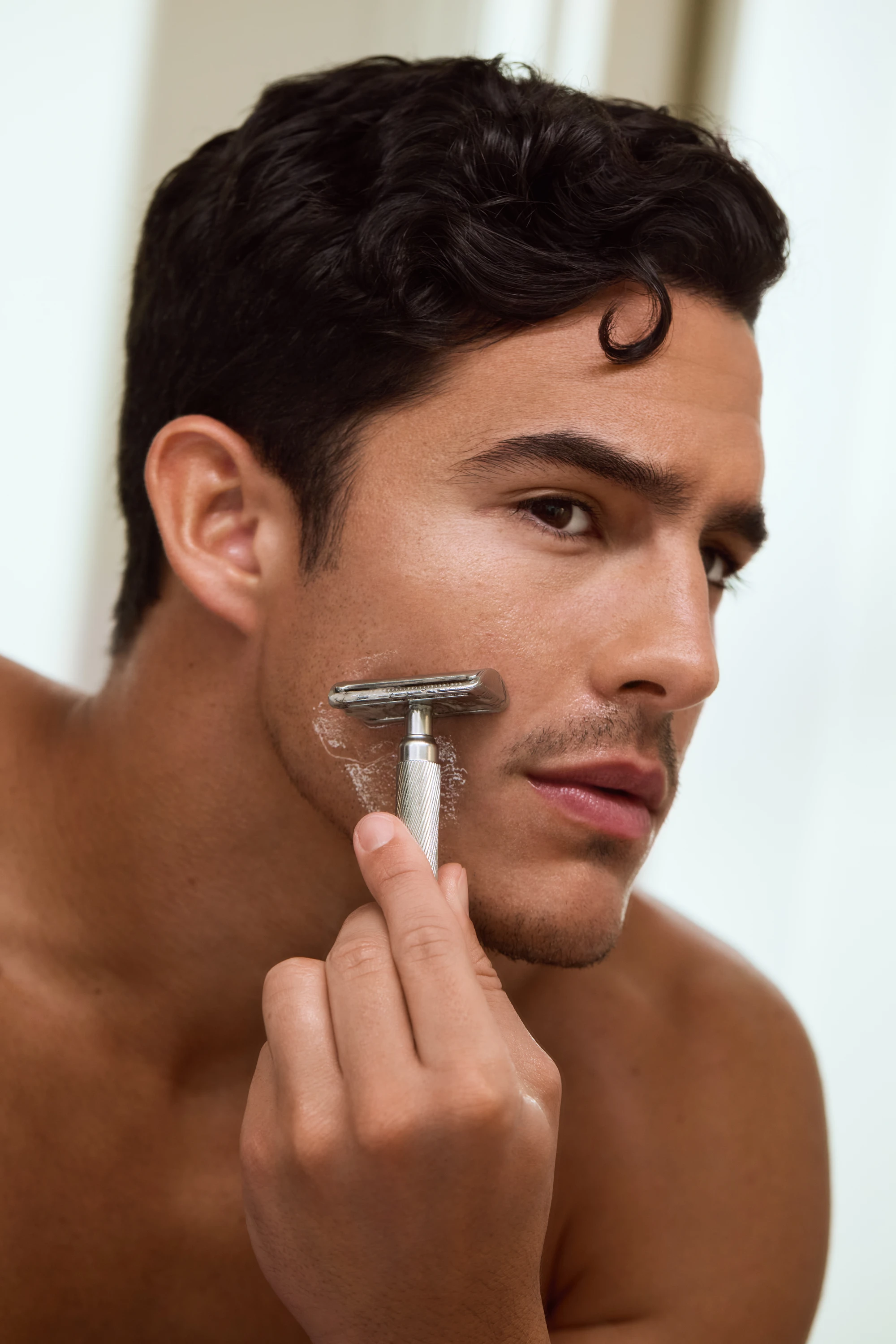 A model shaving his cheek with a razor.