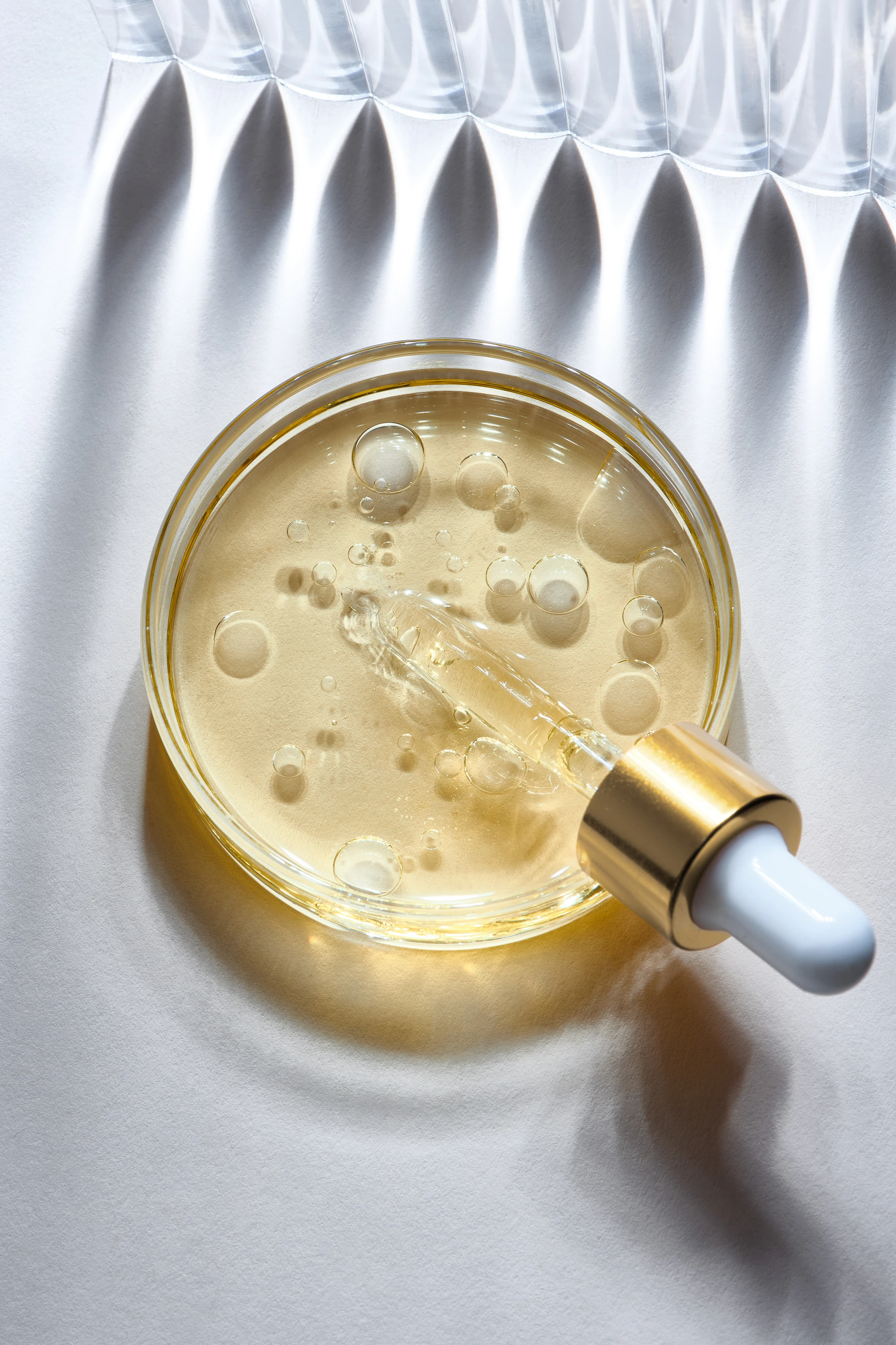 A dish of golden hair oil beside glass dropper tools.