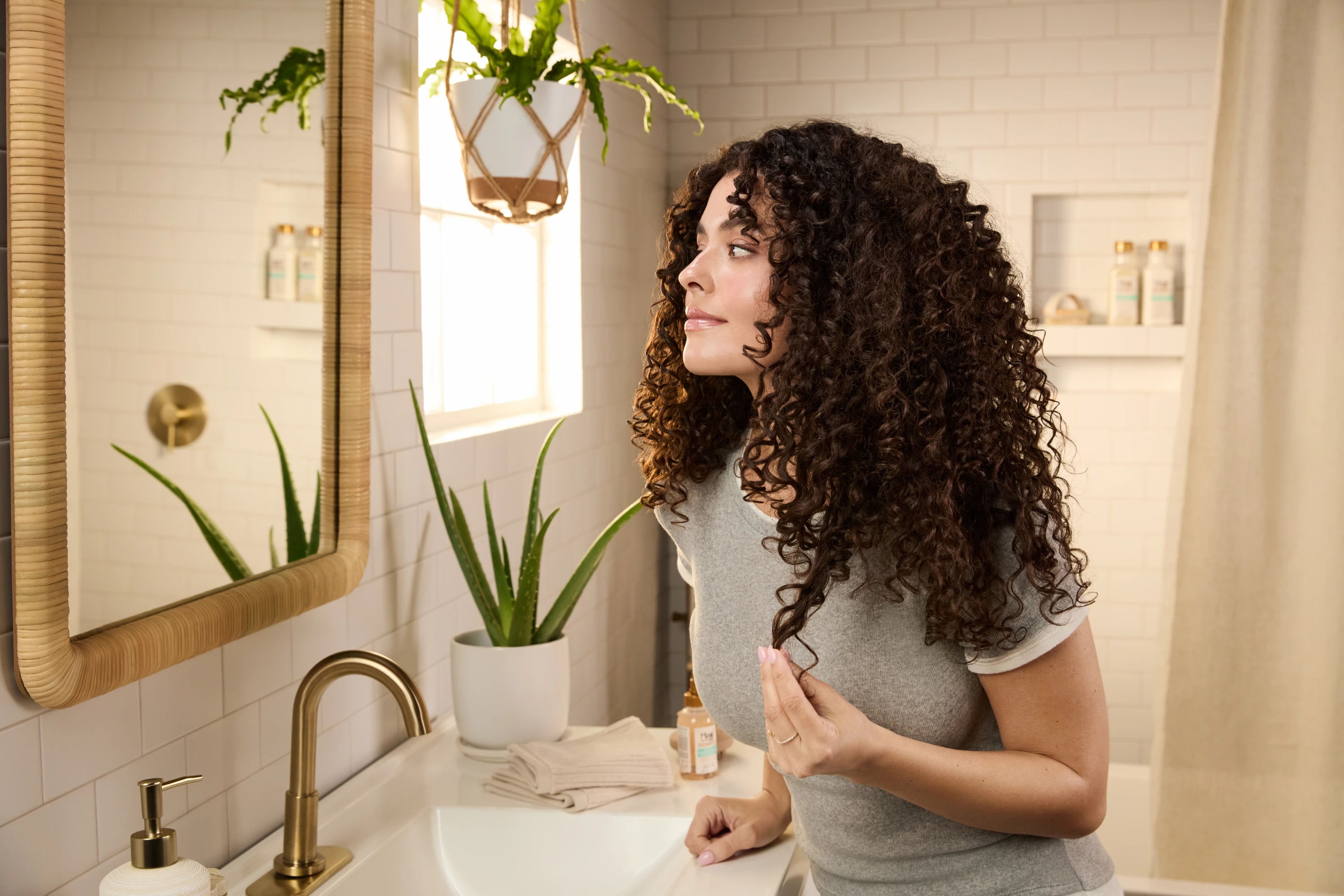 A curly-haired model standing at a bathroom mirror.