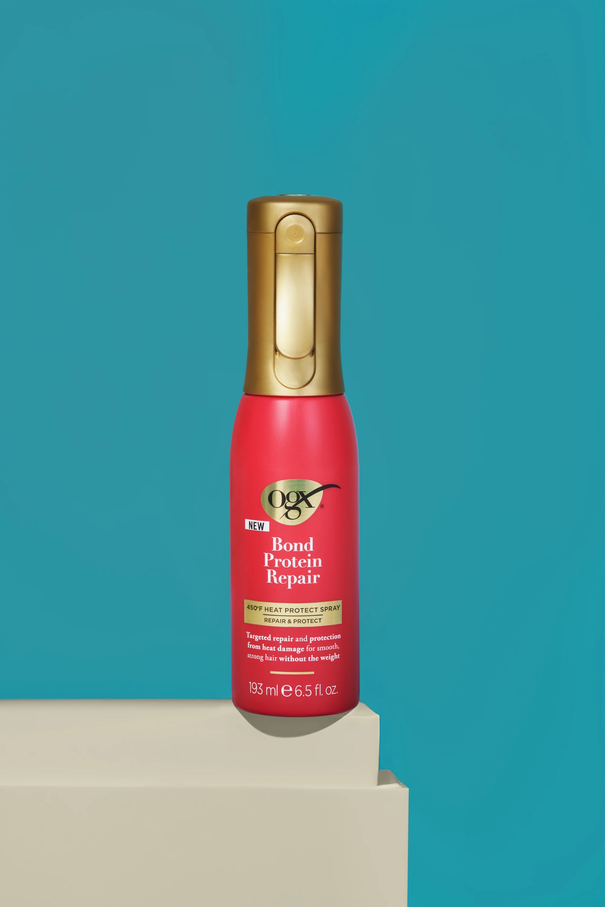 A red OGX spray bottle against a teal background.