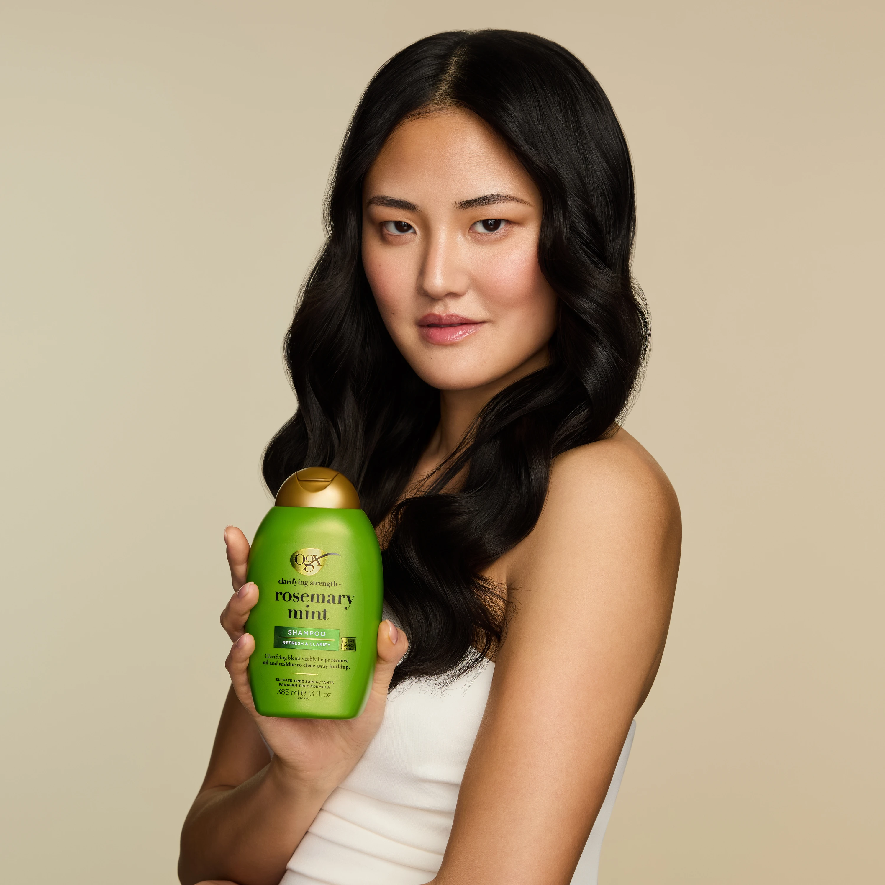 A model holding a green OGX bottle beside glossy dark hair.
