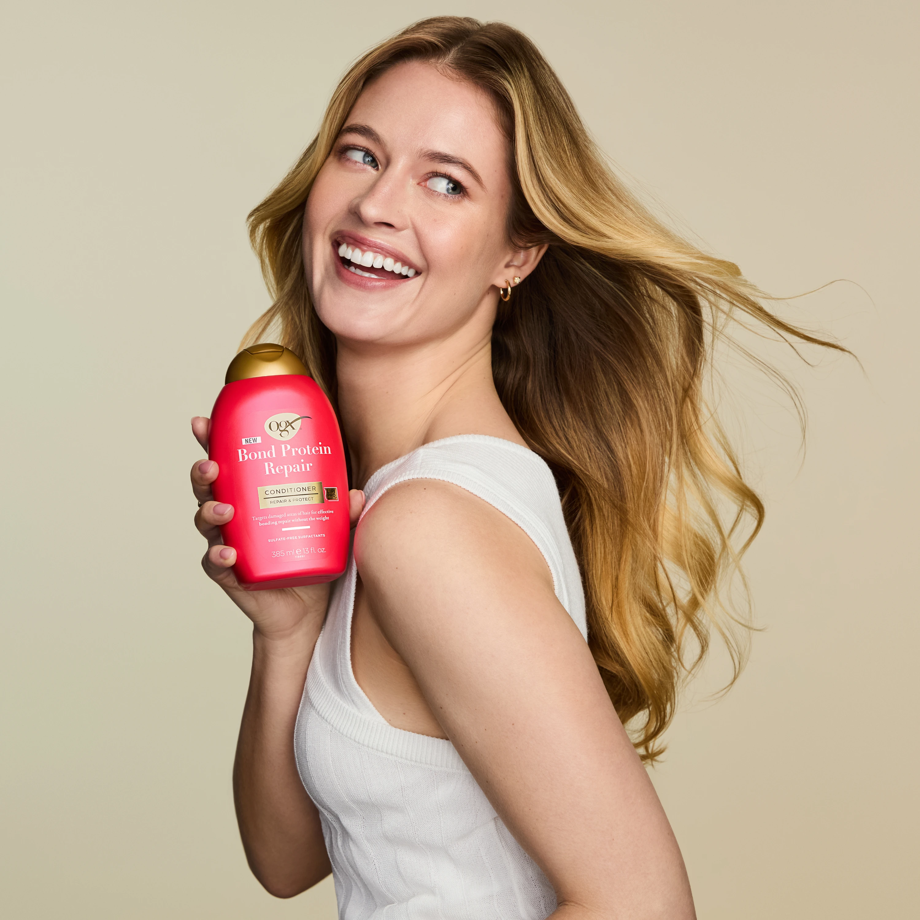A model holding a red OGX bottle beside wavy blonde hair.