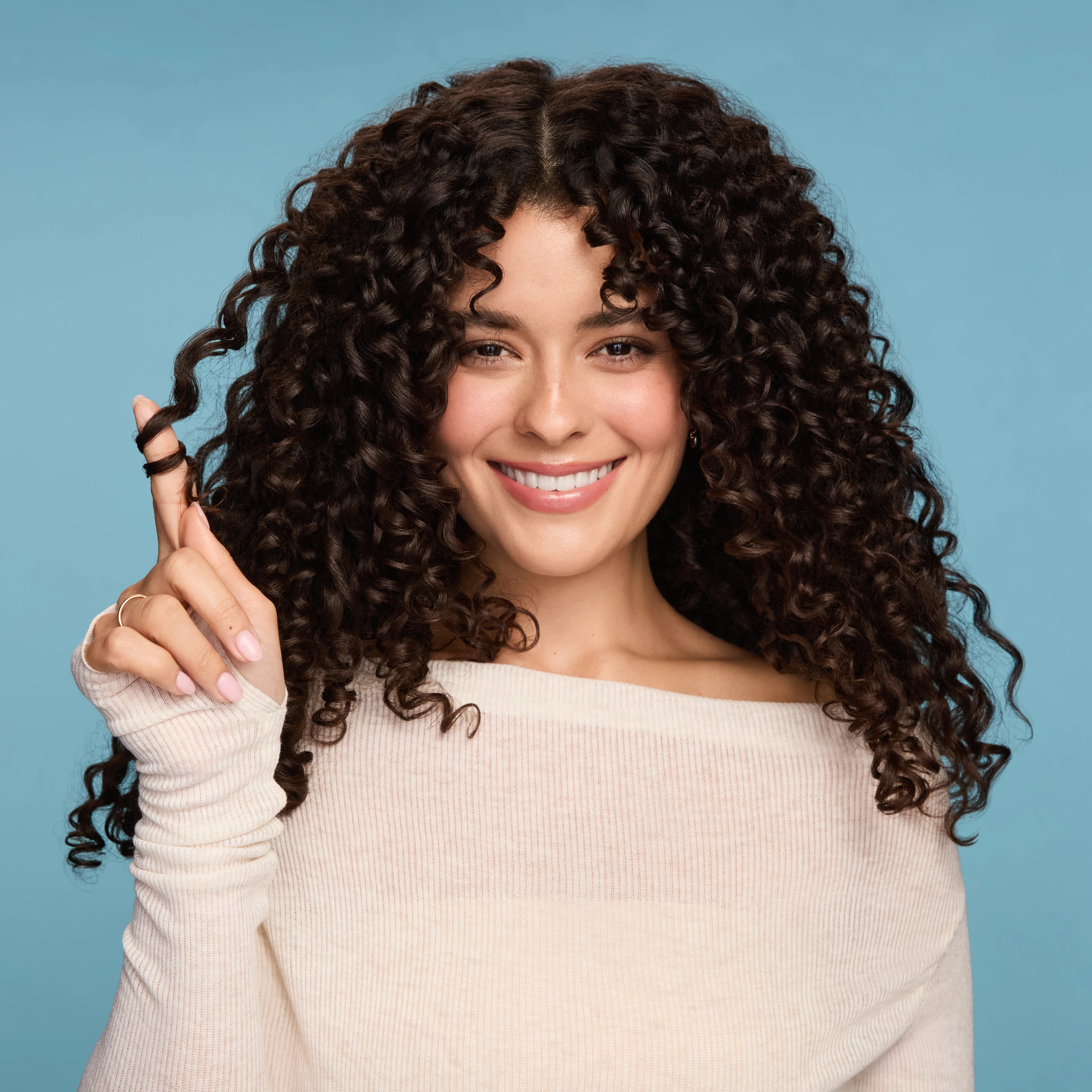 A smiling model holding a curl between her fingers.