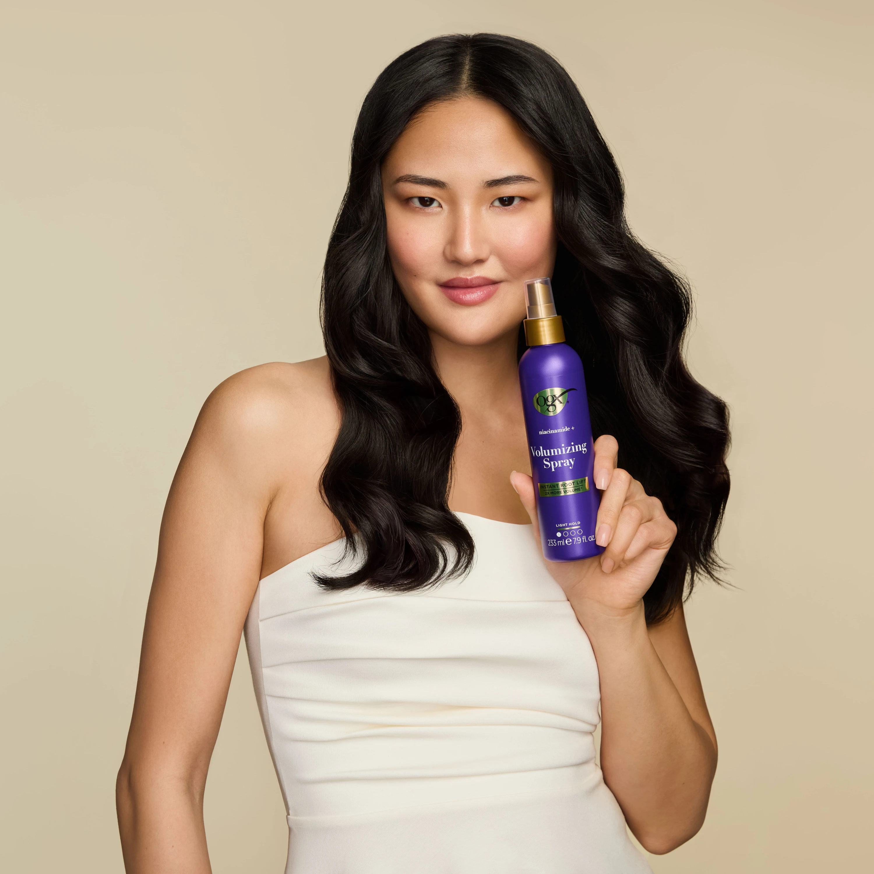 A smiling model holding a purple OGX spray bottle.