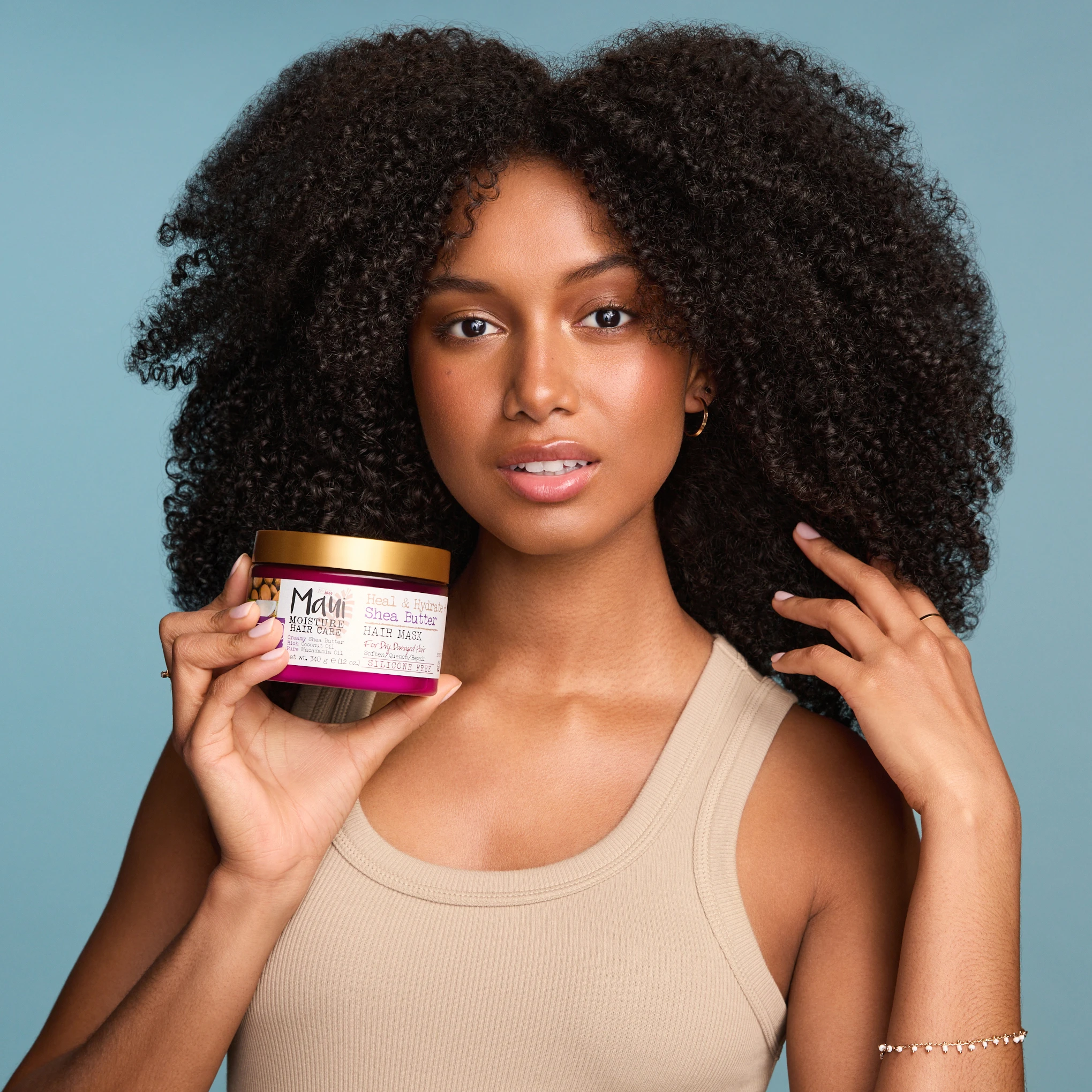 A model with natural curls holding a Maui Moisture jar.