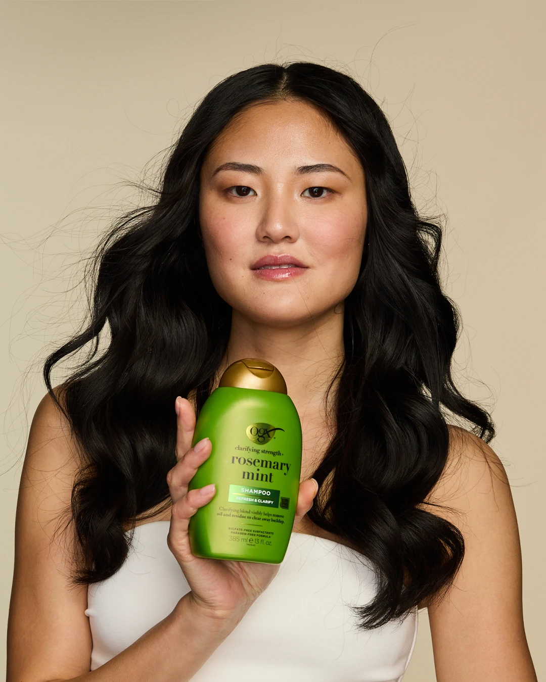A model holding a green OGX bottle beside long dark hair.