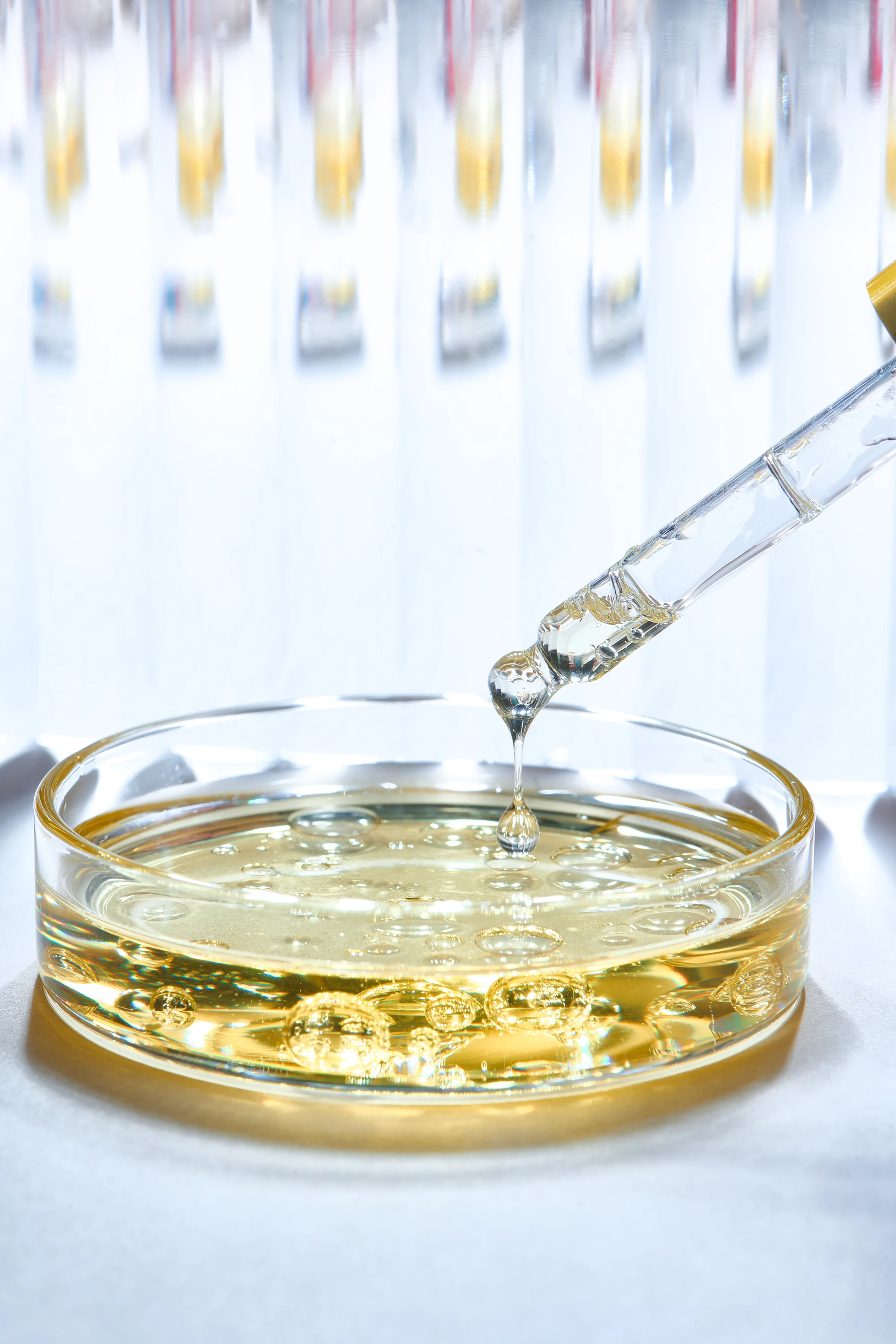 A dropper releasing liquid into a dish of hair oil.