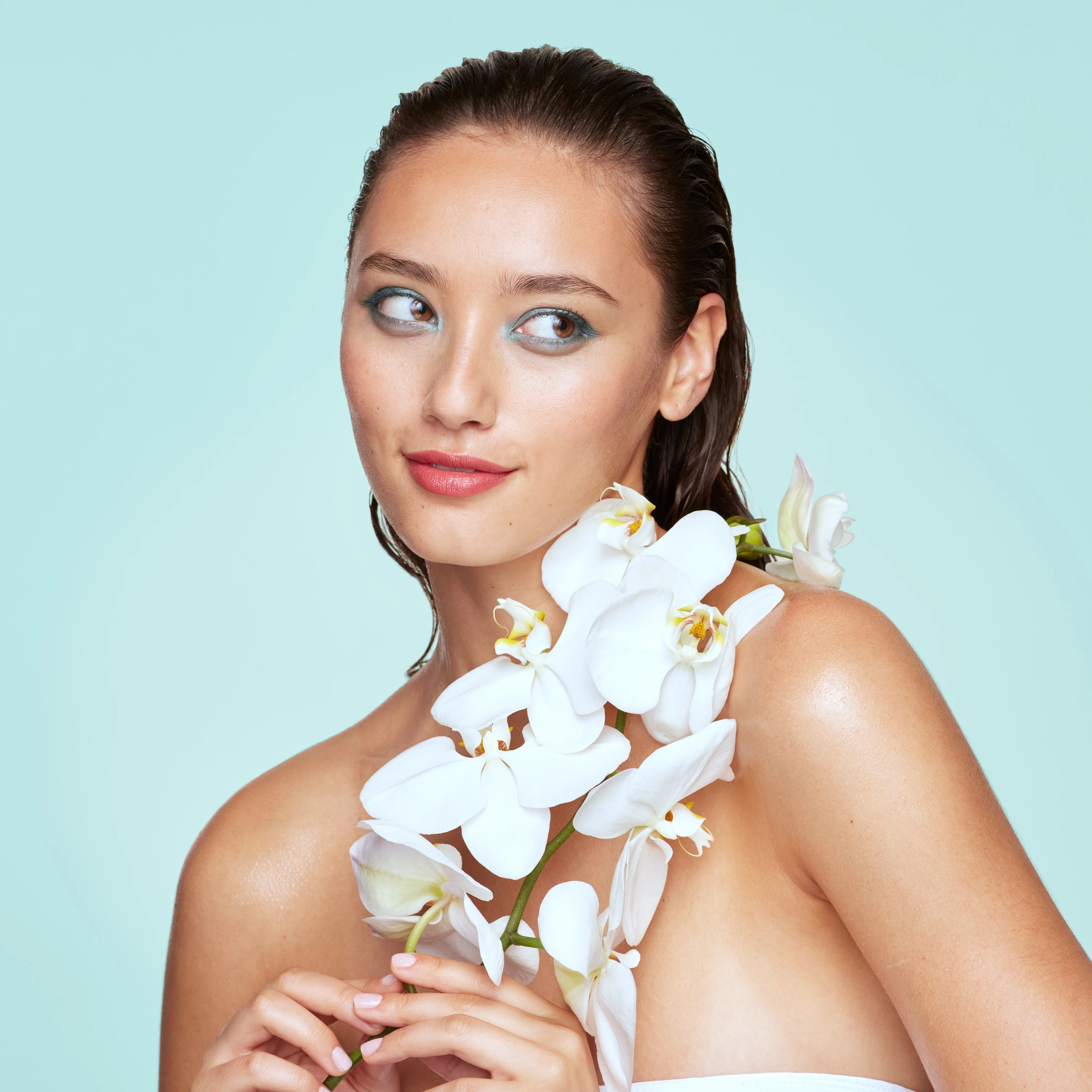 A model posing with white flowers against an aqua background.