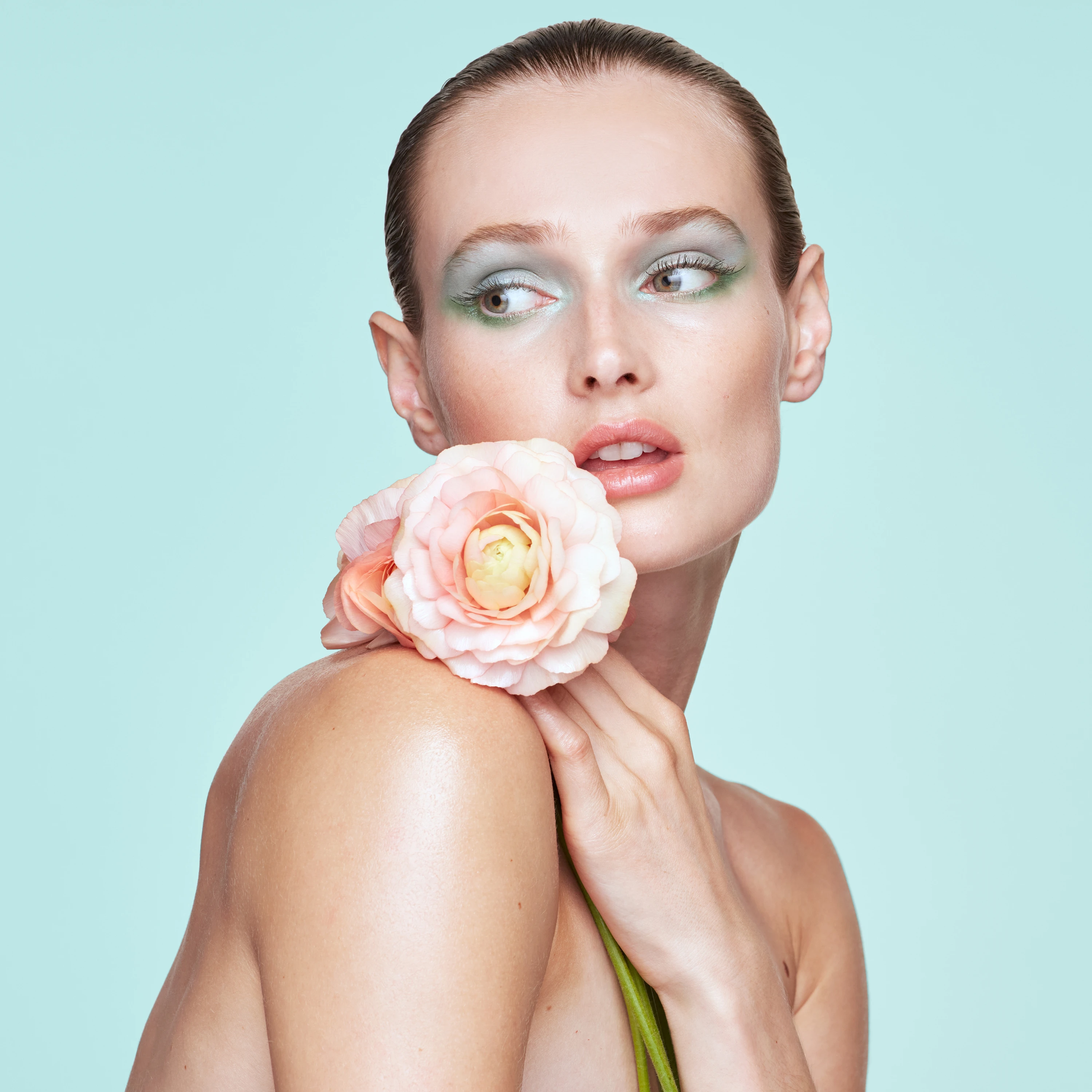 A model holding a pale pink flower beside her face.