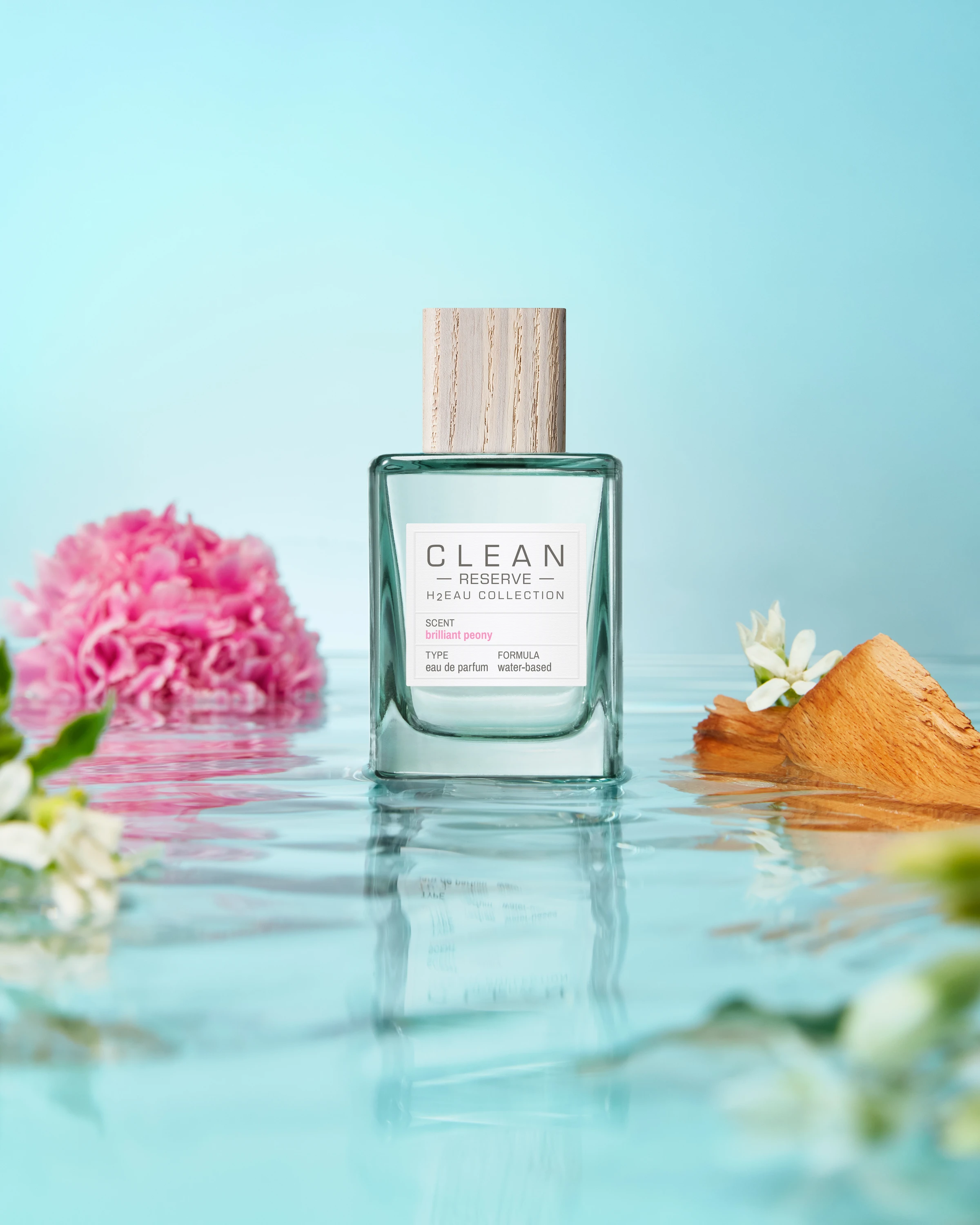 A Clean Reserve bottle and flowers on a reflective watery surface.