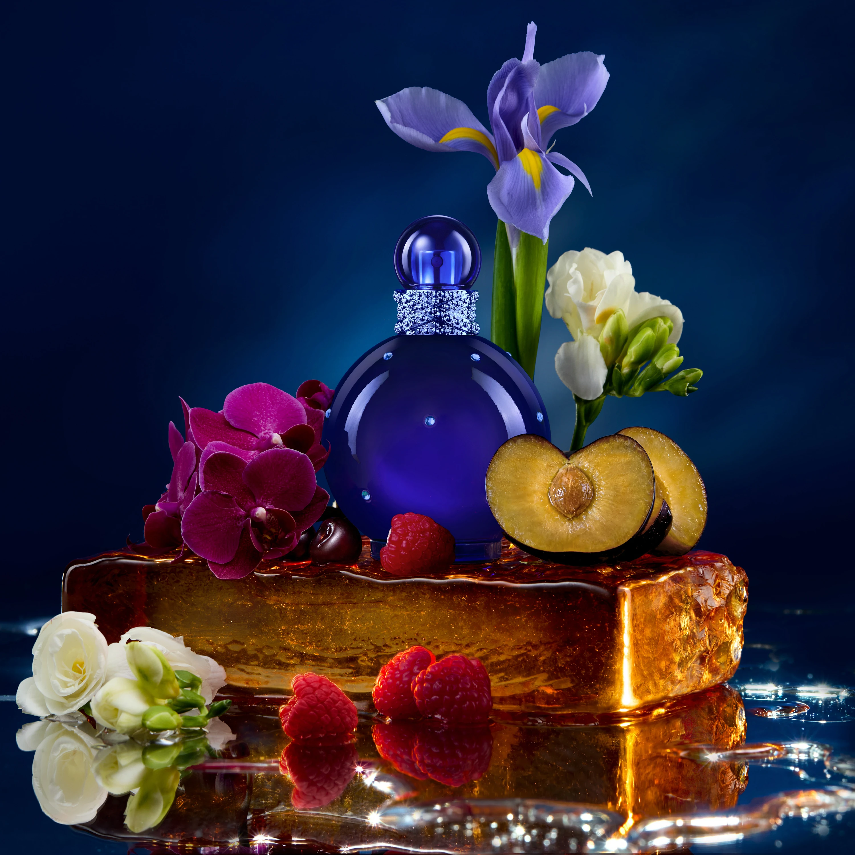 A blue Britney Spears fragrance bottle surrounded by flowers and fruit.