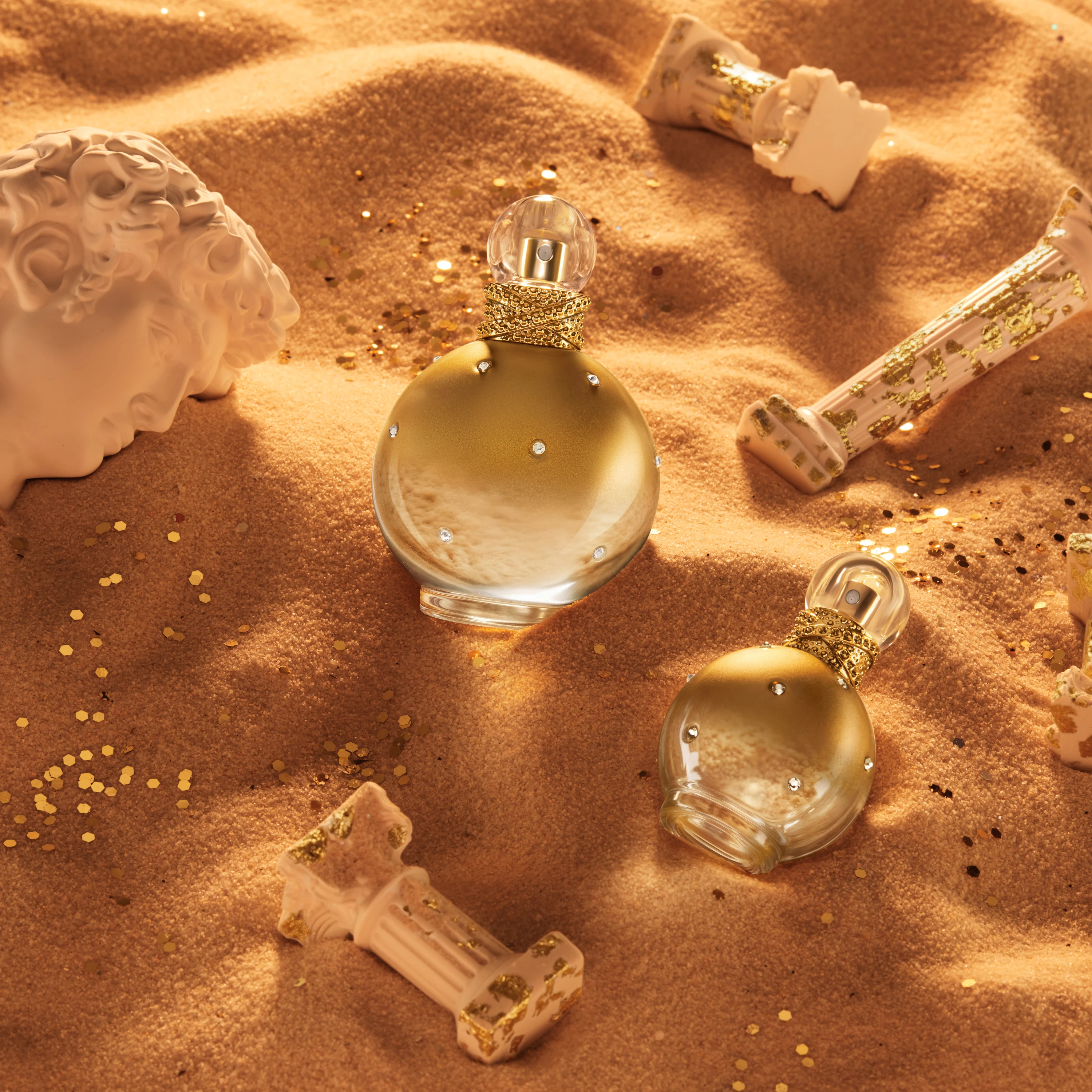 Gold fragrance bottles arranged on sand.