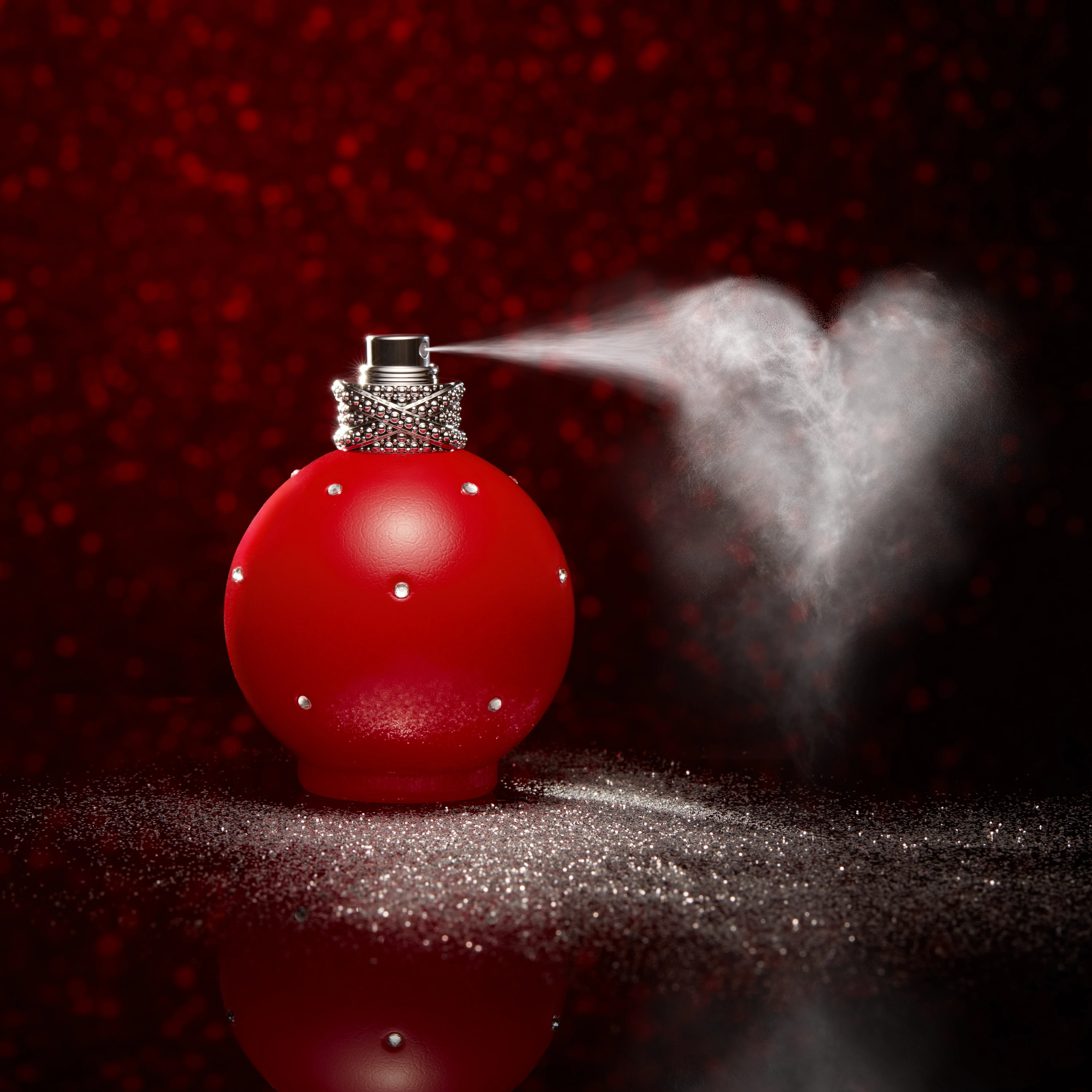 A red round fragrance bottle emitting a spray.