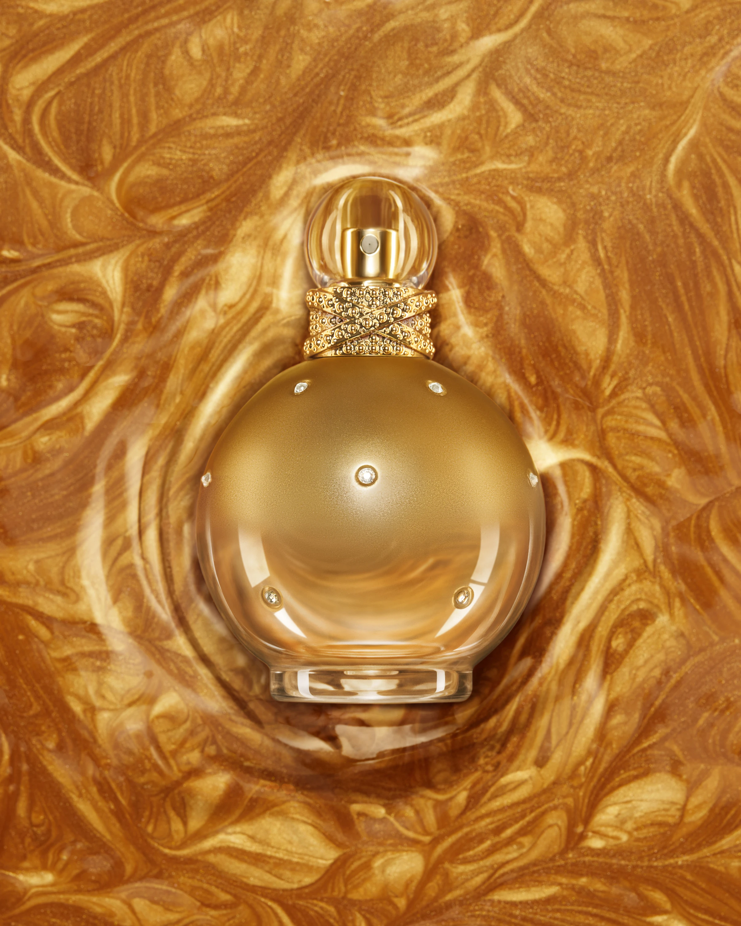 A gold fragrance bottle nestled in rippled gold fabric.
