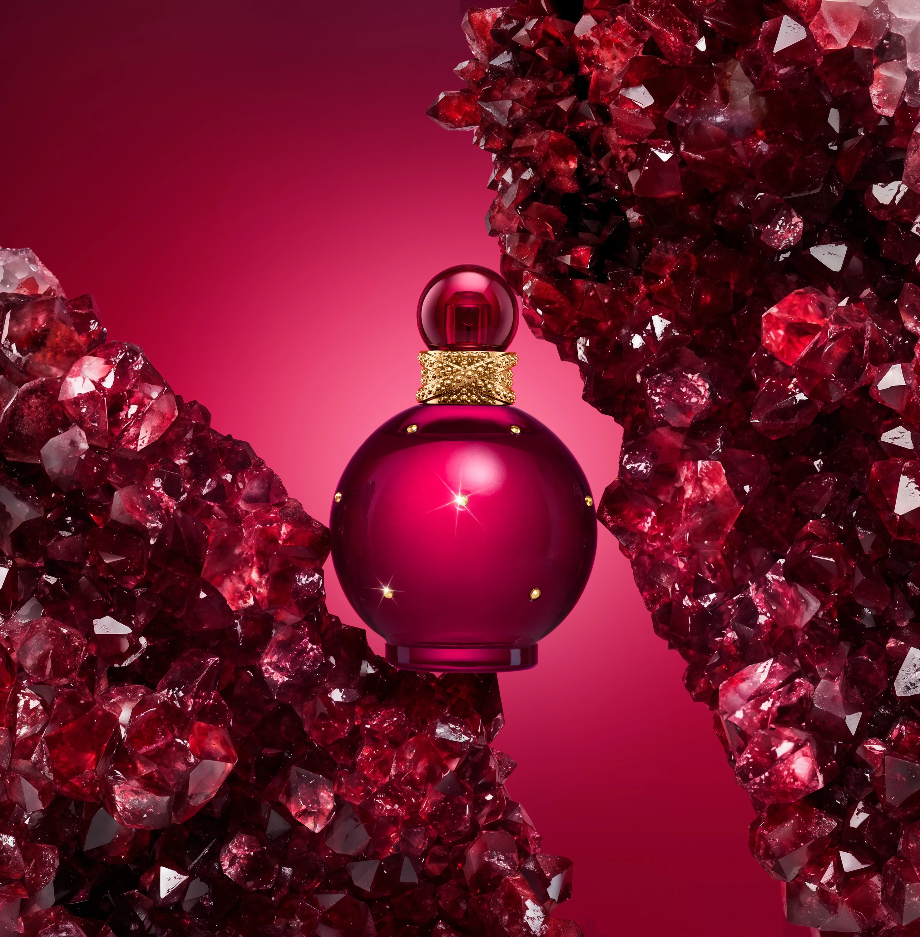 A dark pink fragrance bottle surrounded by sparkling pink shapes.
