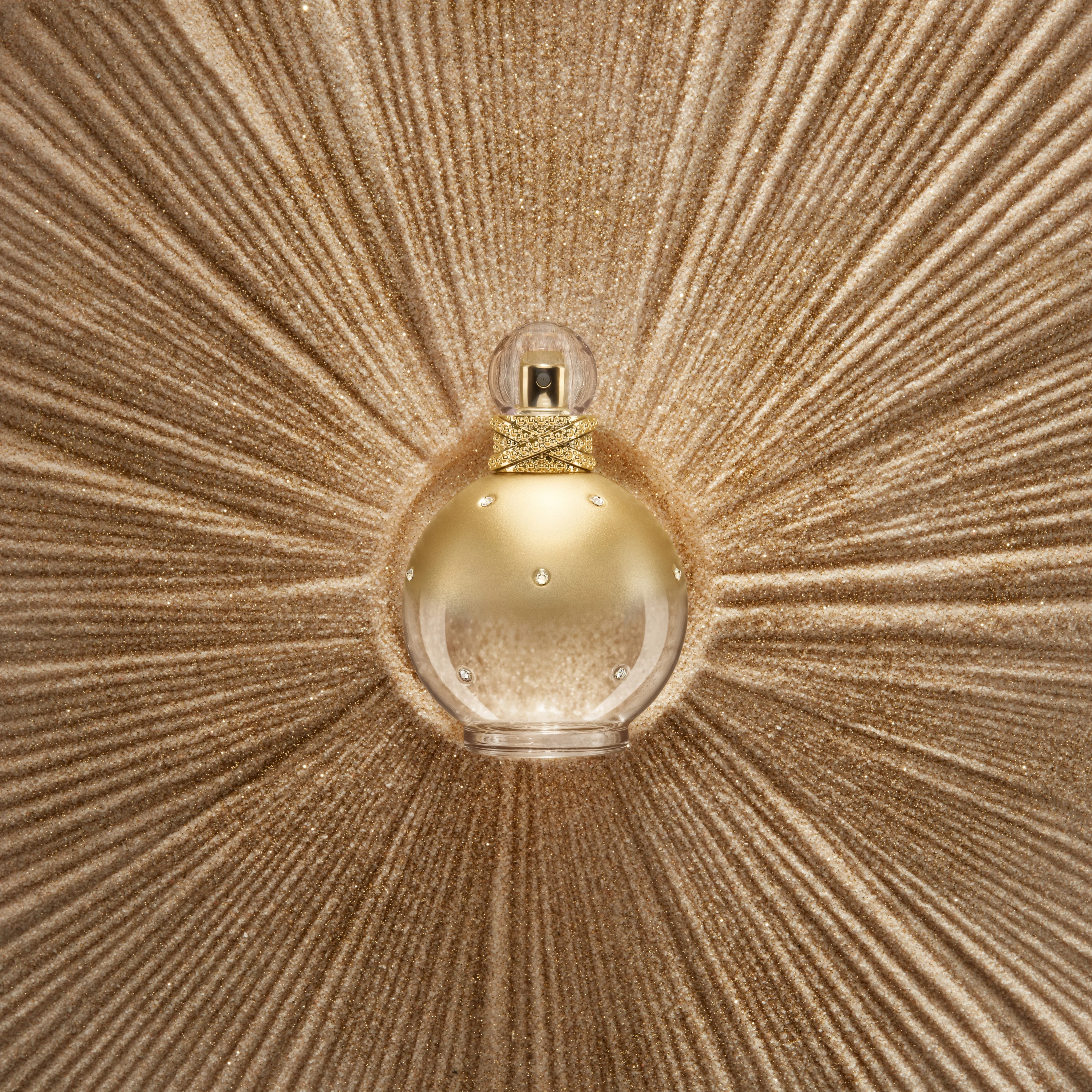 A gold round fragrance bottle centered on radiating textured lines.