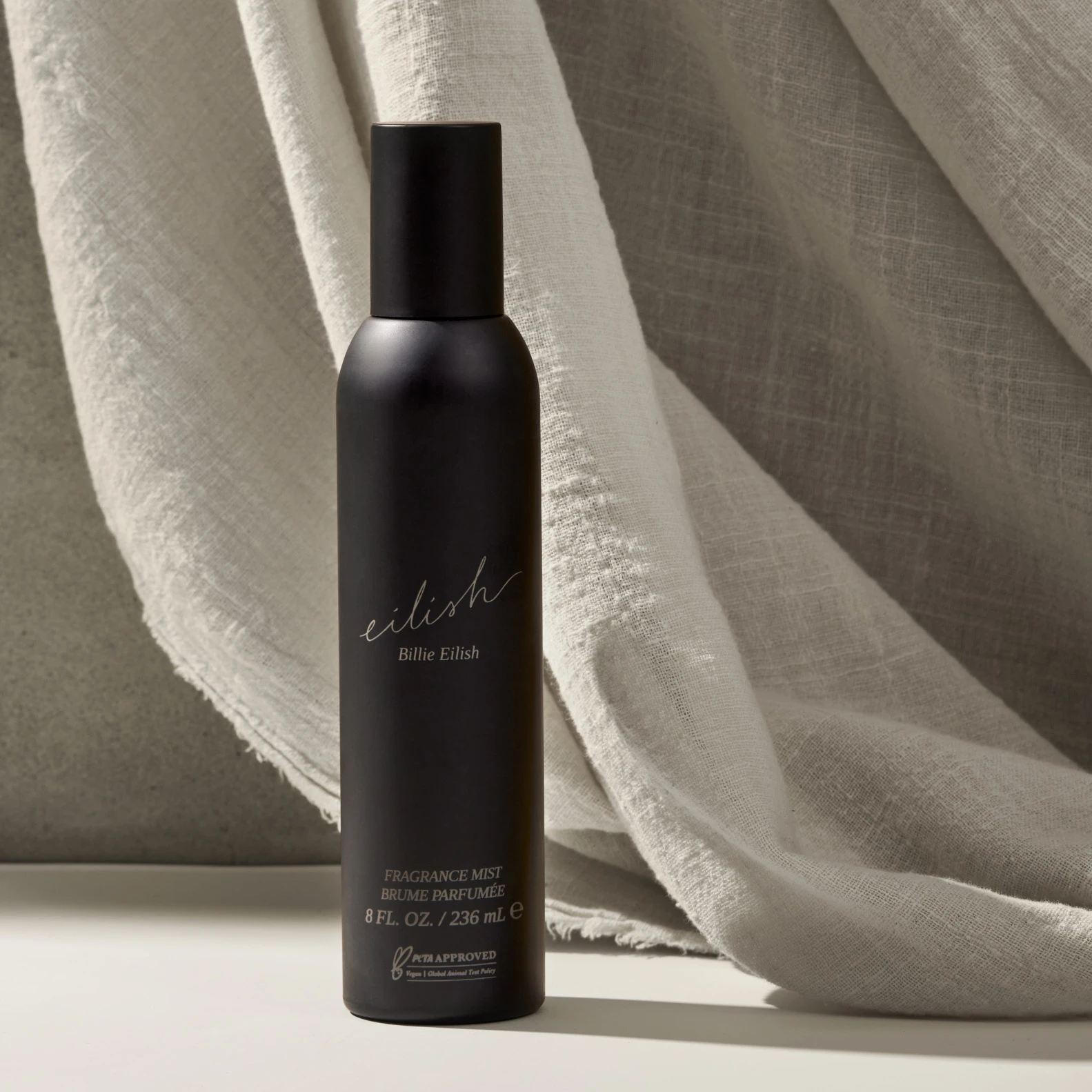 A dark Billie Eilish spray bottle beside pale fabric.