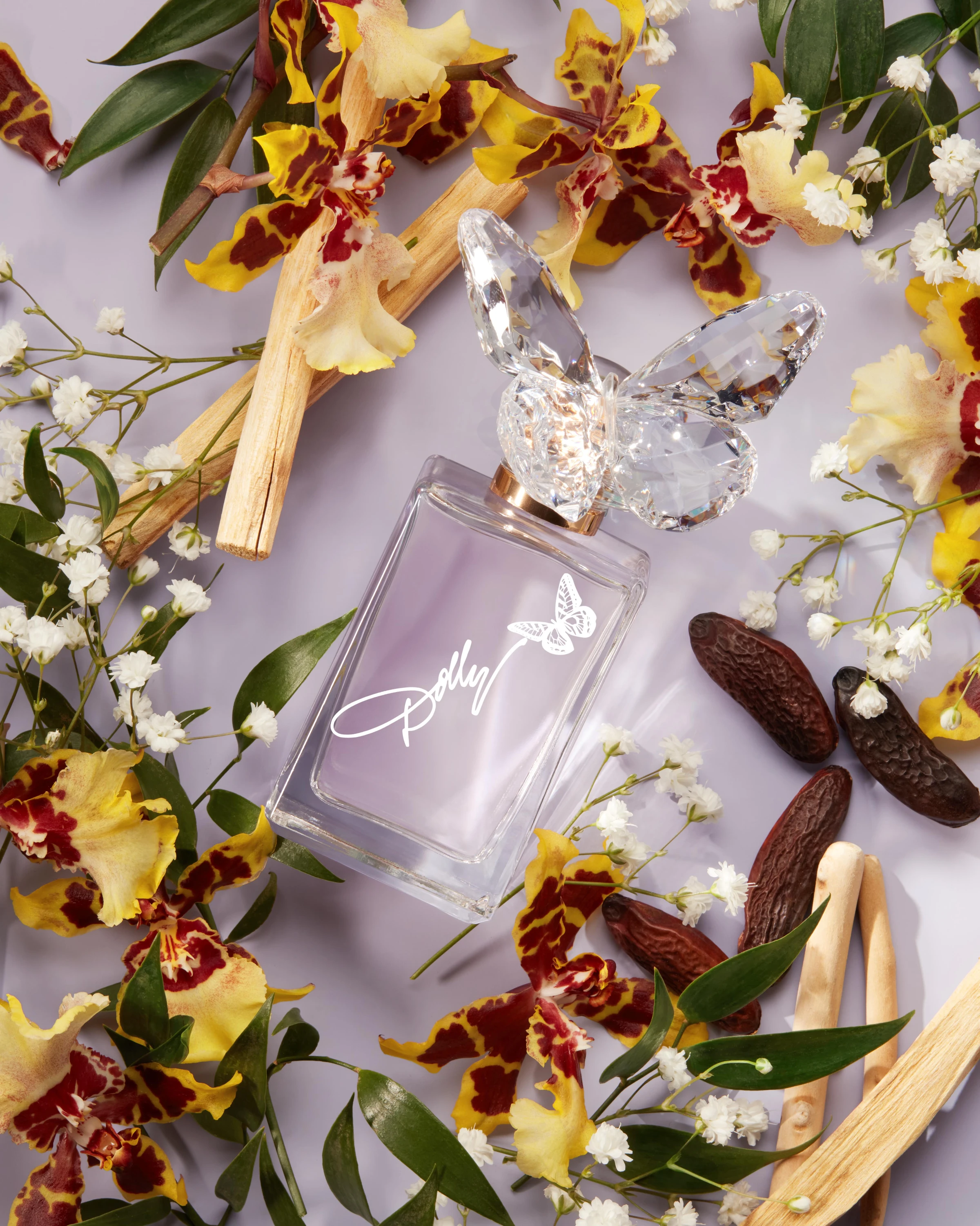 A pale purple Dolly Parton bottle surrounded by flowers and vanilla pods.