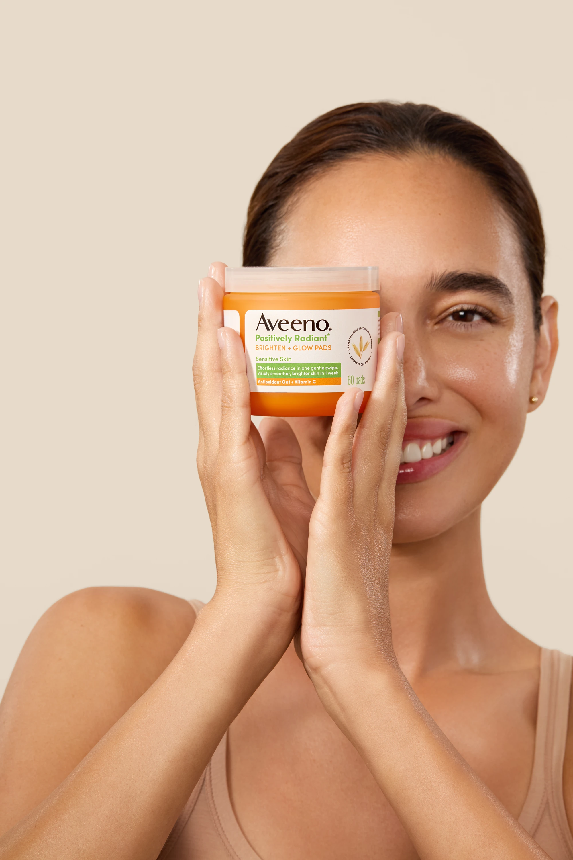 A smiling model holding an Aveeno jar beside her face.