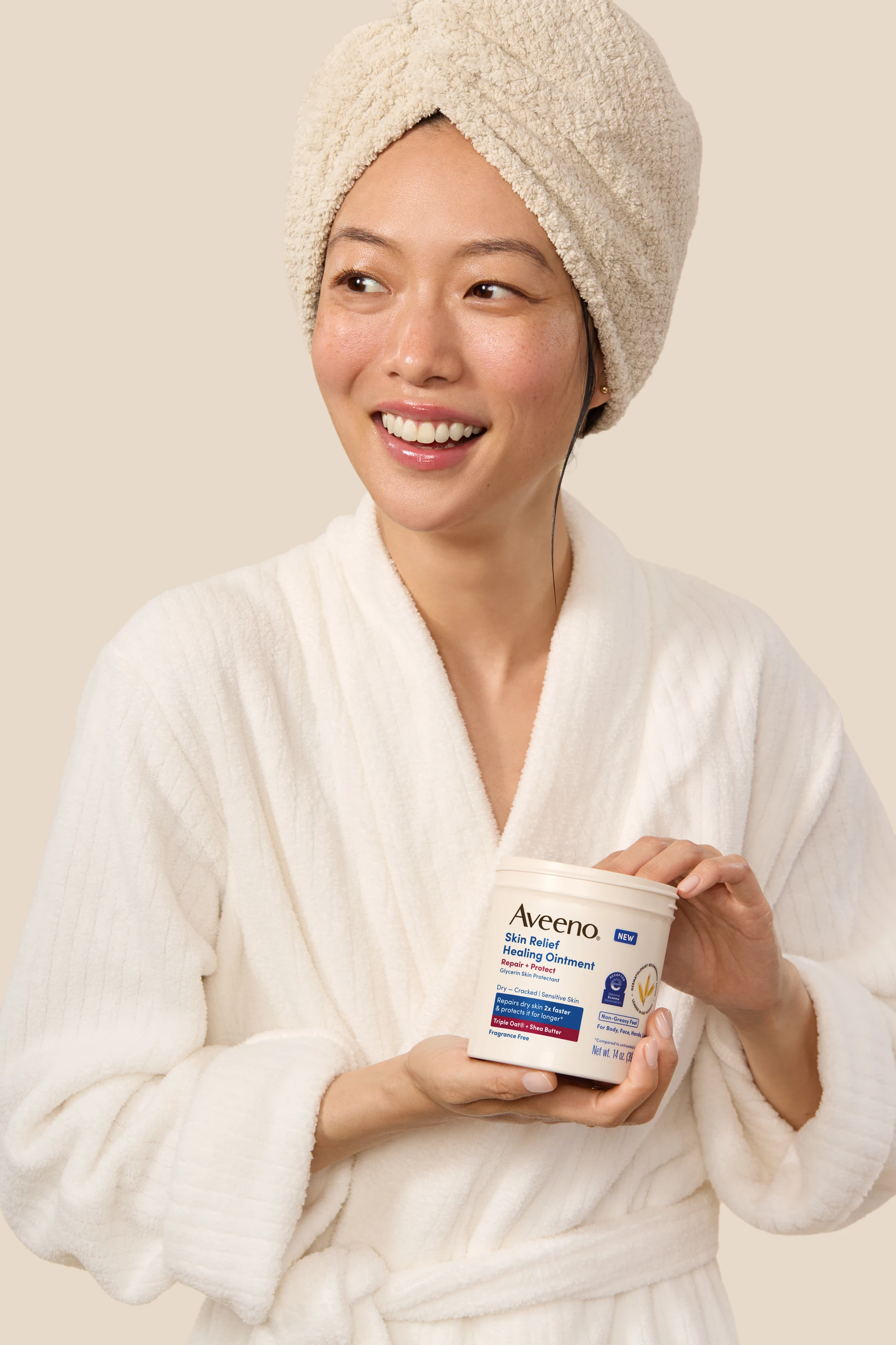 A model with a towel around her hair holding an Aveeno jar.