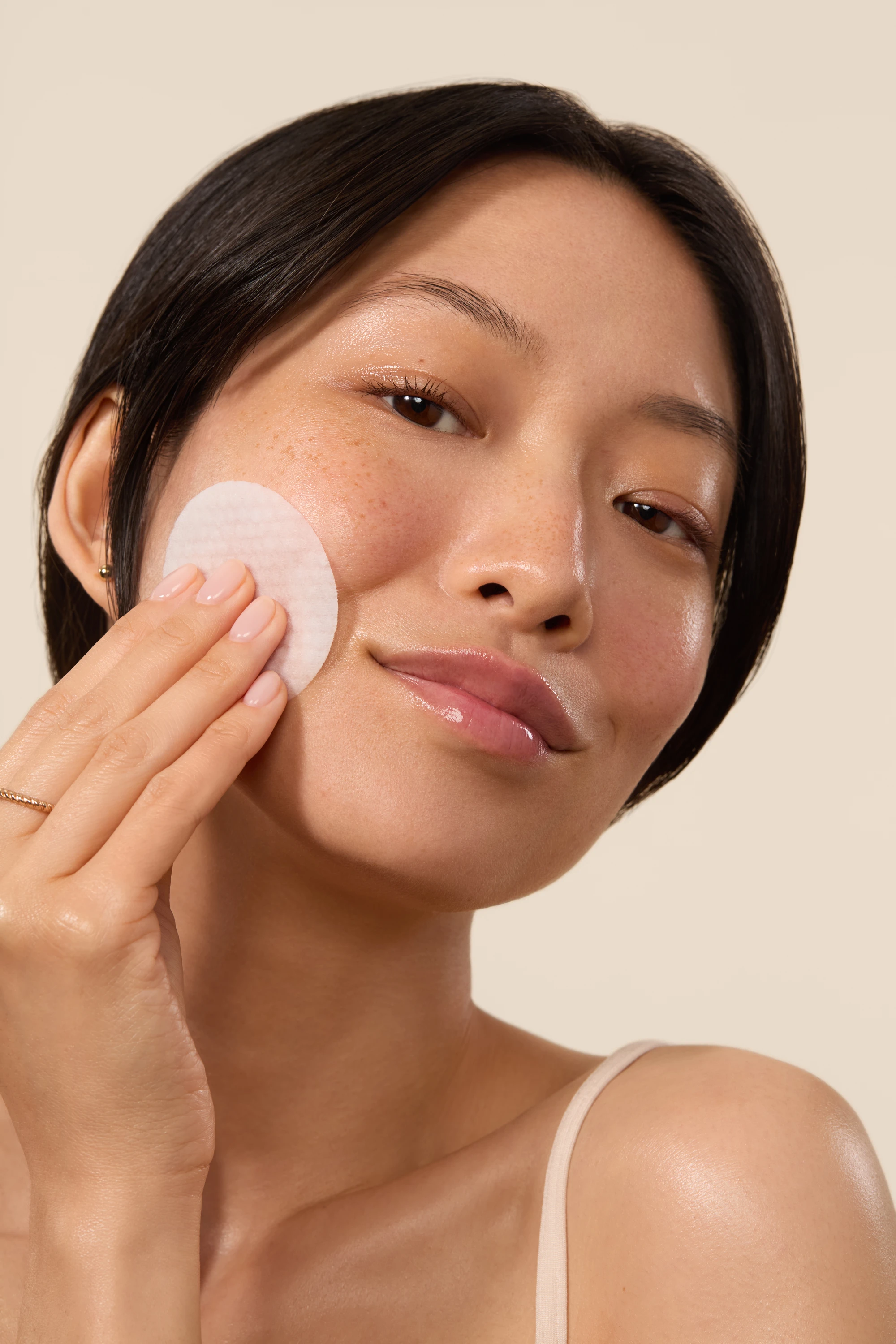 A model wiping her cheek with a cotton pad.