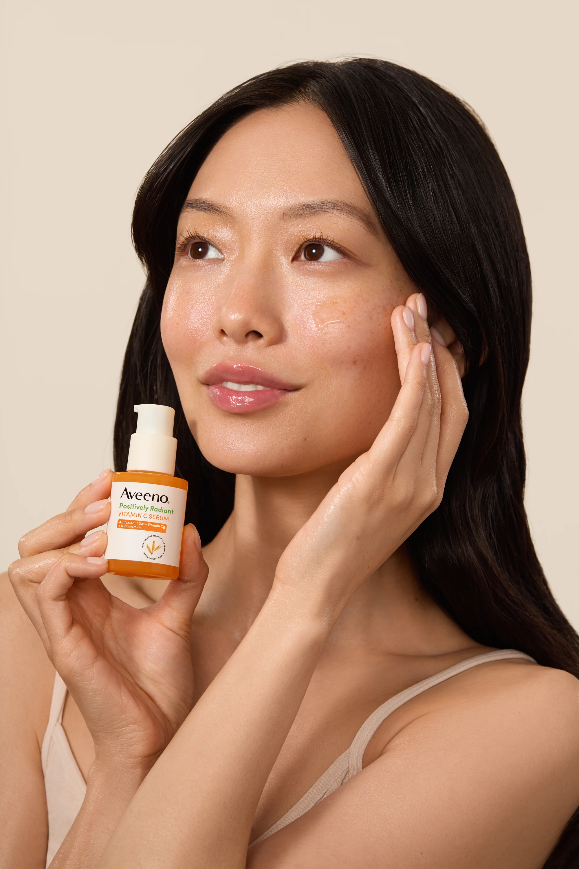 A model holding Aveeno serum while touching her cheek.