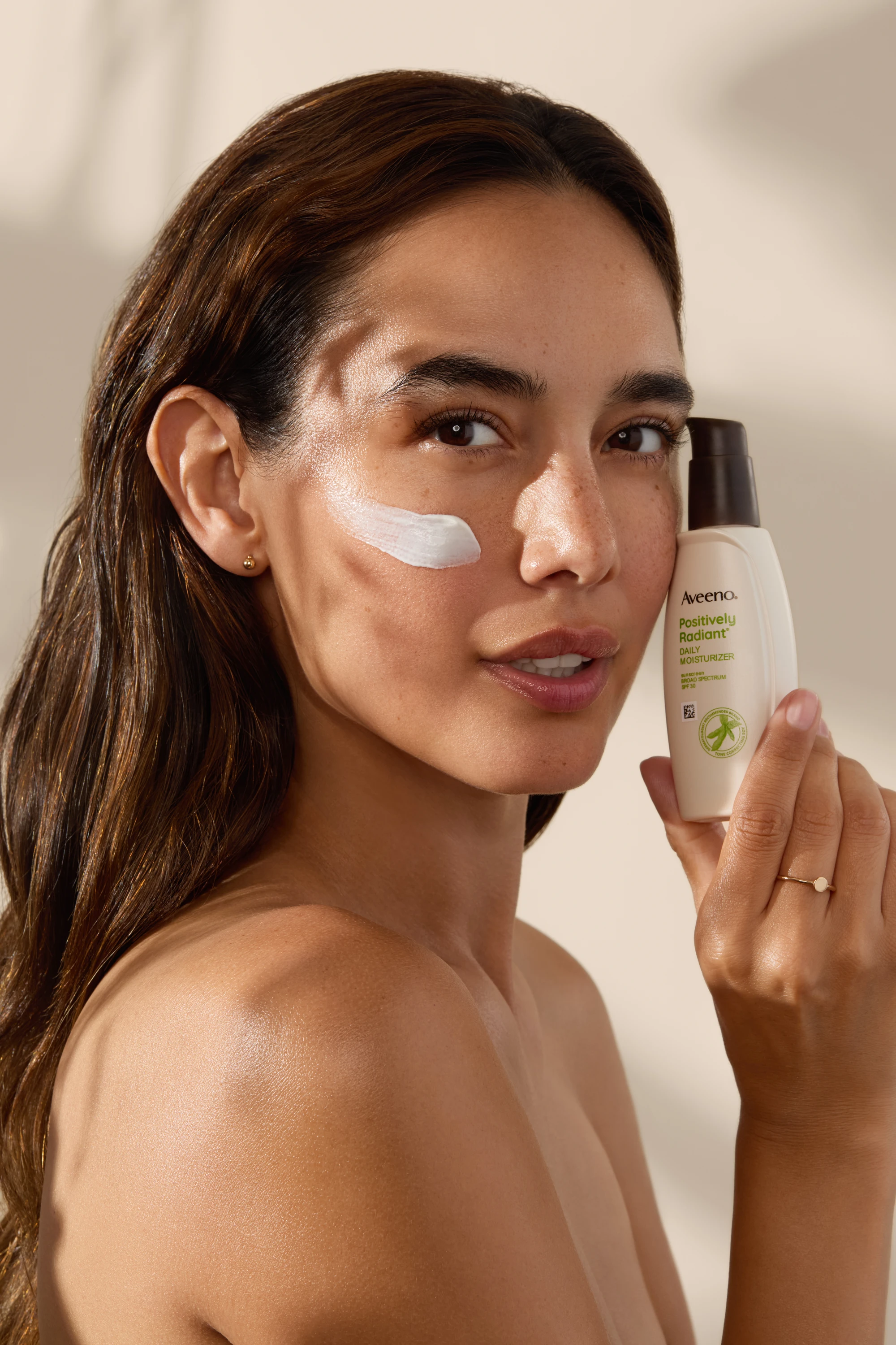 A model holding an Aveeno bottle with cream dotted on her face.